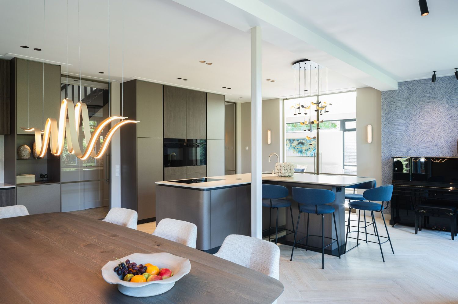 Modern open concept kitchen and dining area with gray cabinetry, wood floors and statement lighting fixture.