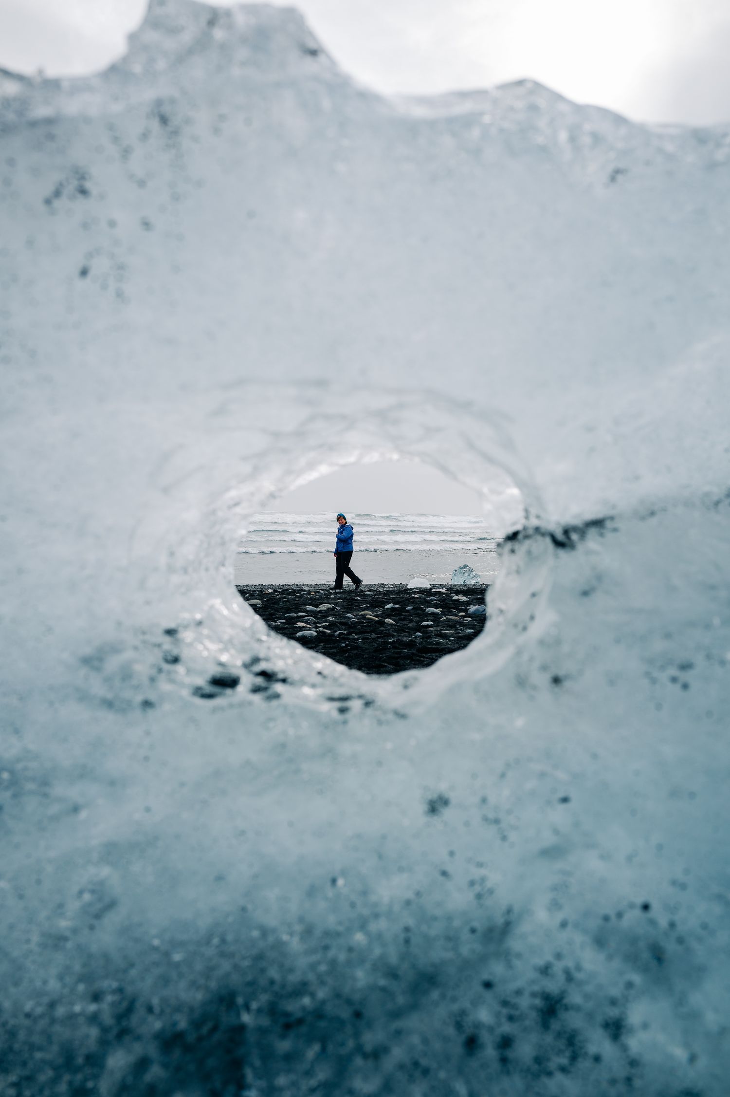 A person explores a massive ice cave formation with dark patches against a stark white glacial background.