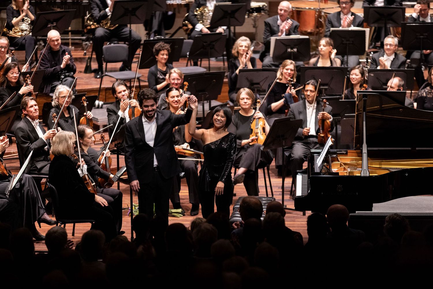Symphony orchestra performs on stage with conductor leading musicians and piano soloist during classical concert.