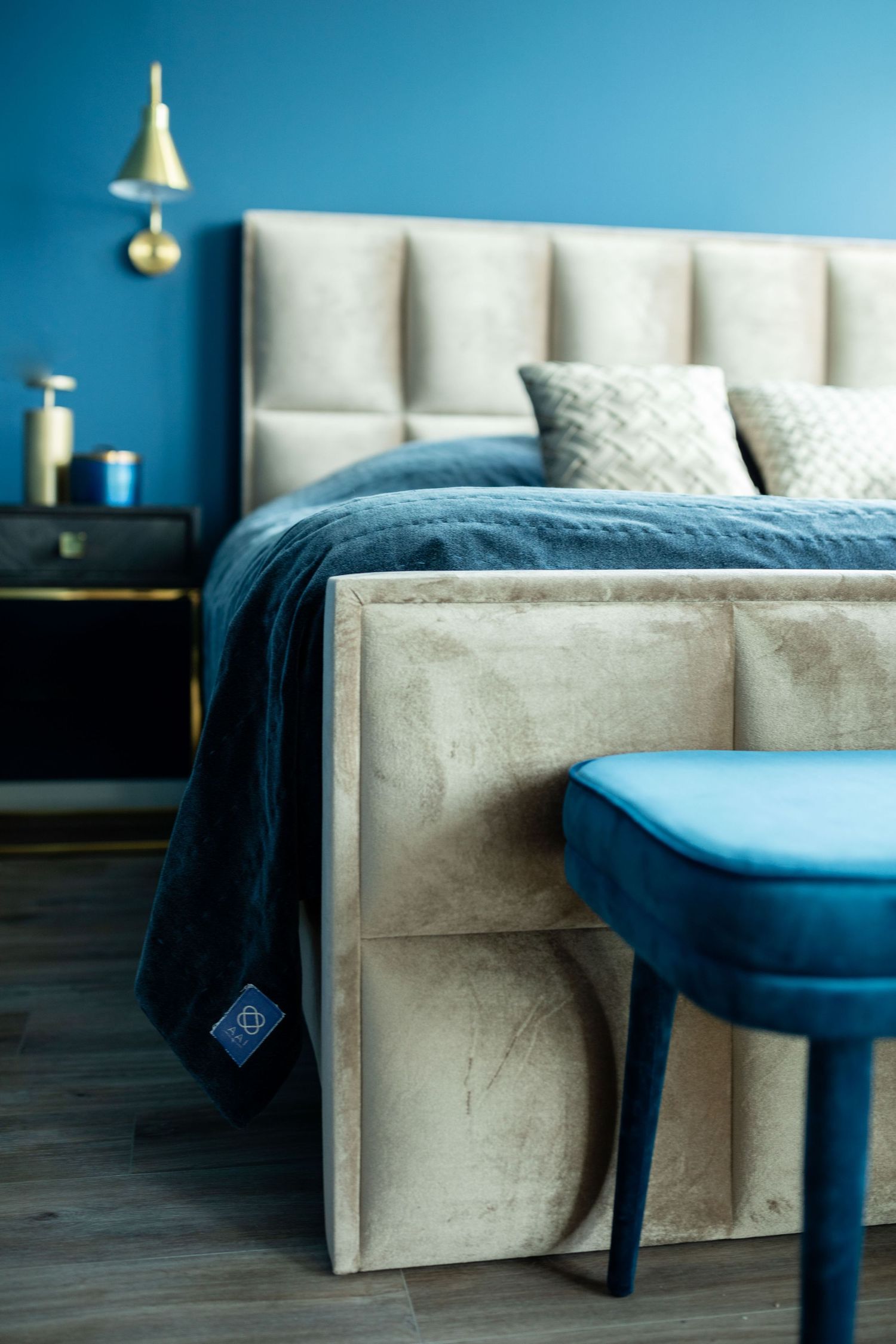 Modern bedroom interior with beige upholstered headboard and blue accents against turquoise walls.