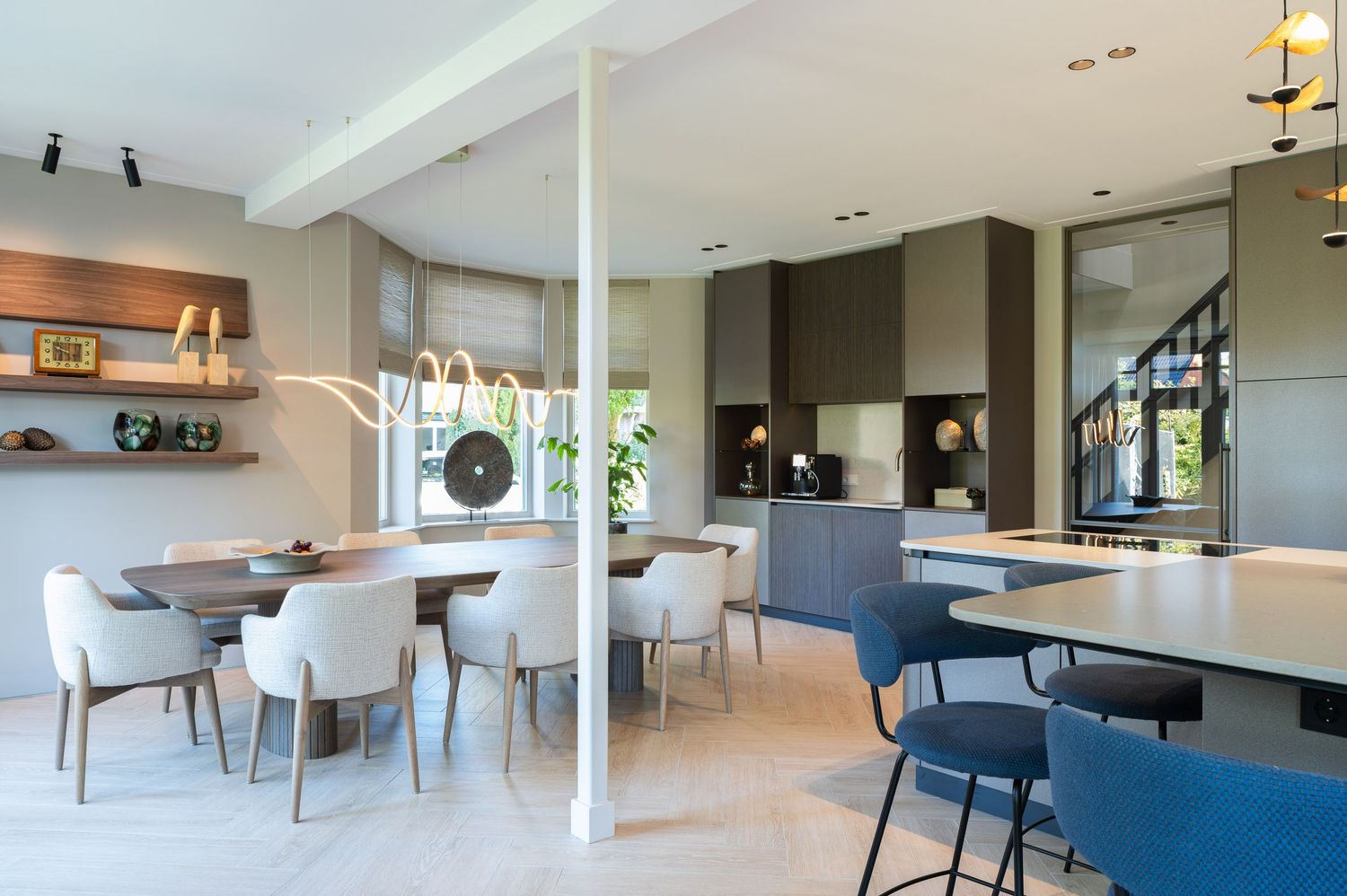 Modern open concept living space features sleek furniture, white walls, and natural light streaming through large windows.