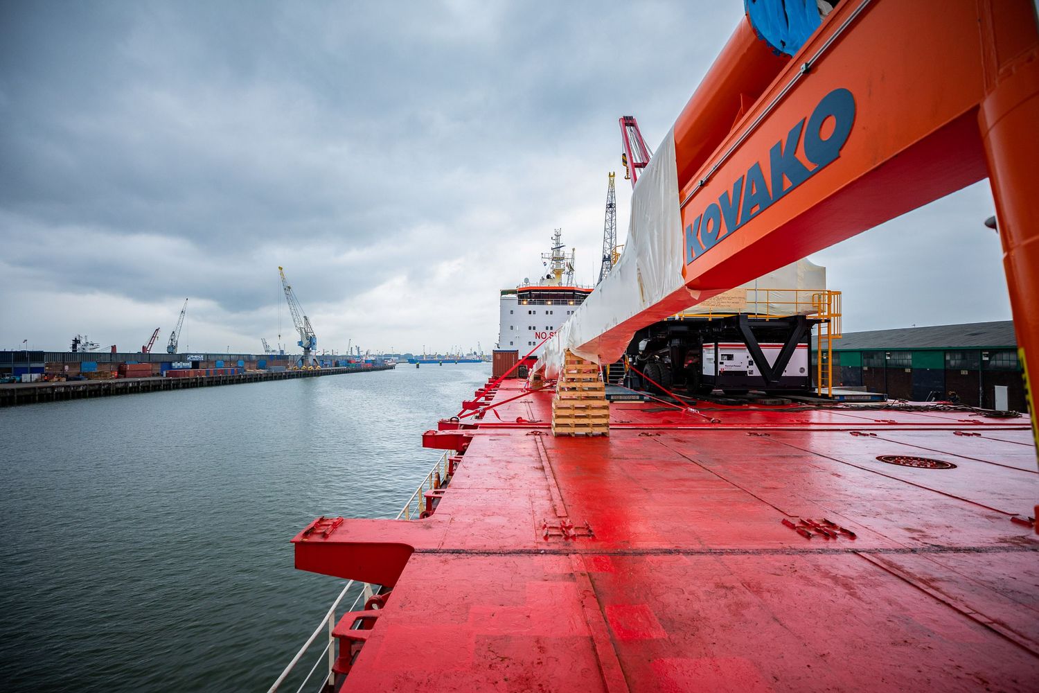 View from red cargo ship deck showing port facilities and cranes in the distance.