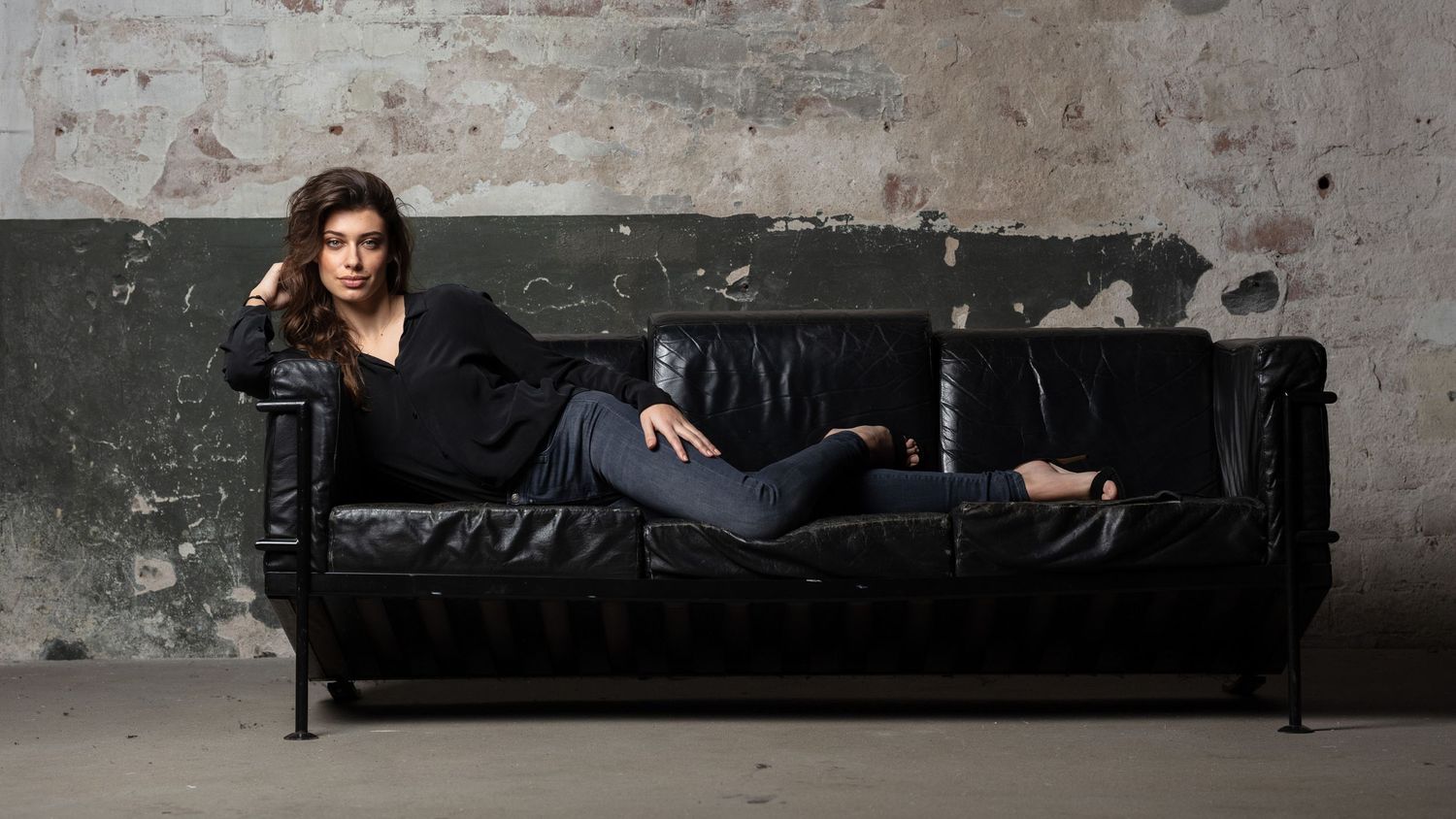 Dark moody interior scene with leather couch against distressed concrete wall.