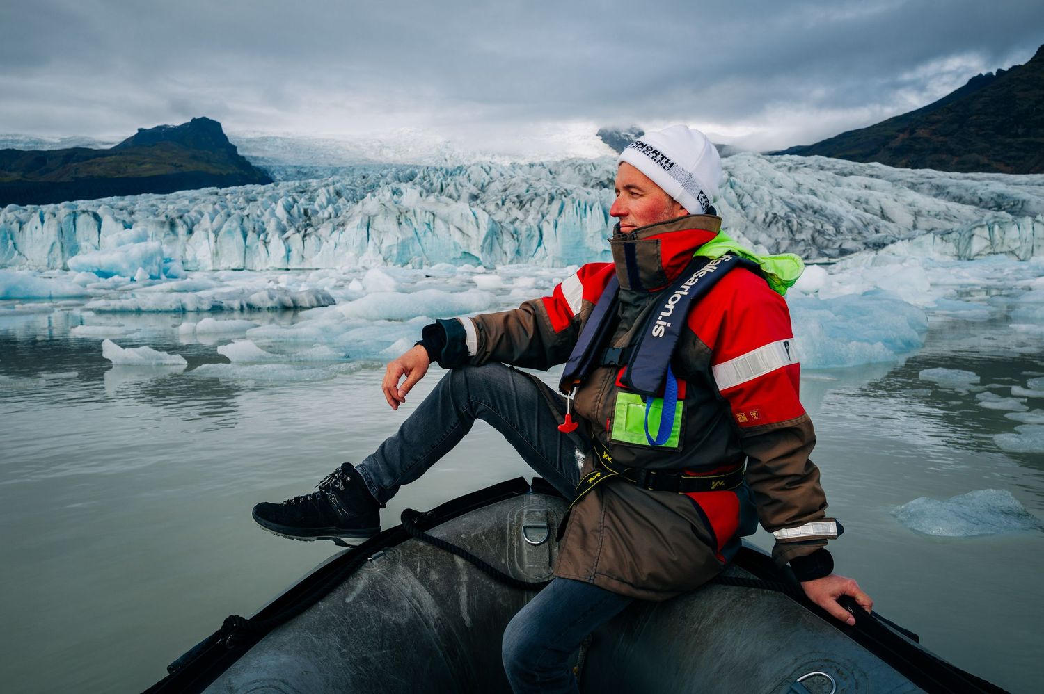 A person in a red jacket explores the dramatic blue ice formations of a massive glacier in Alaska.