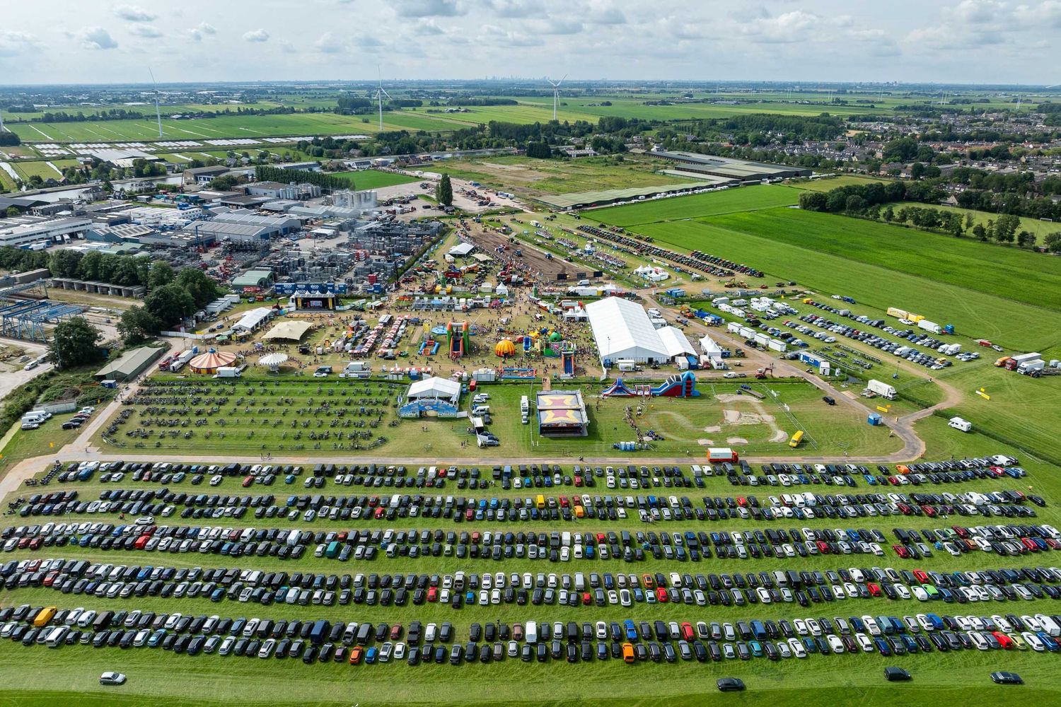 Aerial view of a large outdoor festival with packed parking lots, colorful tents, and green fields in a rural town.