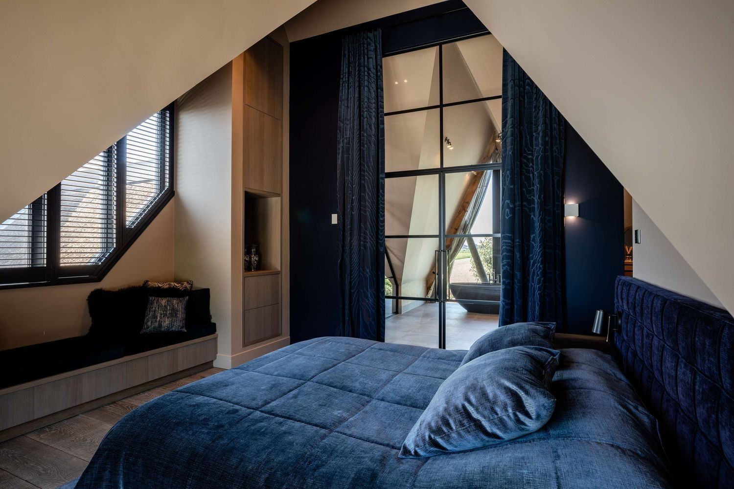 Modern bedroom interior with dark blue curtains and natural light streaming through large windows.