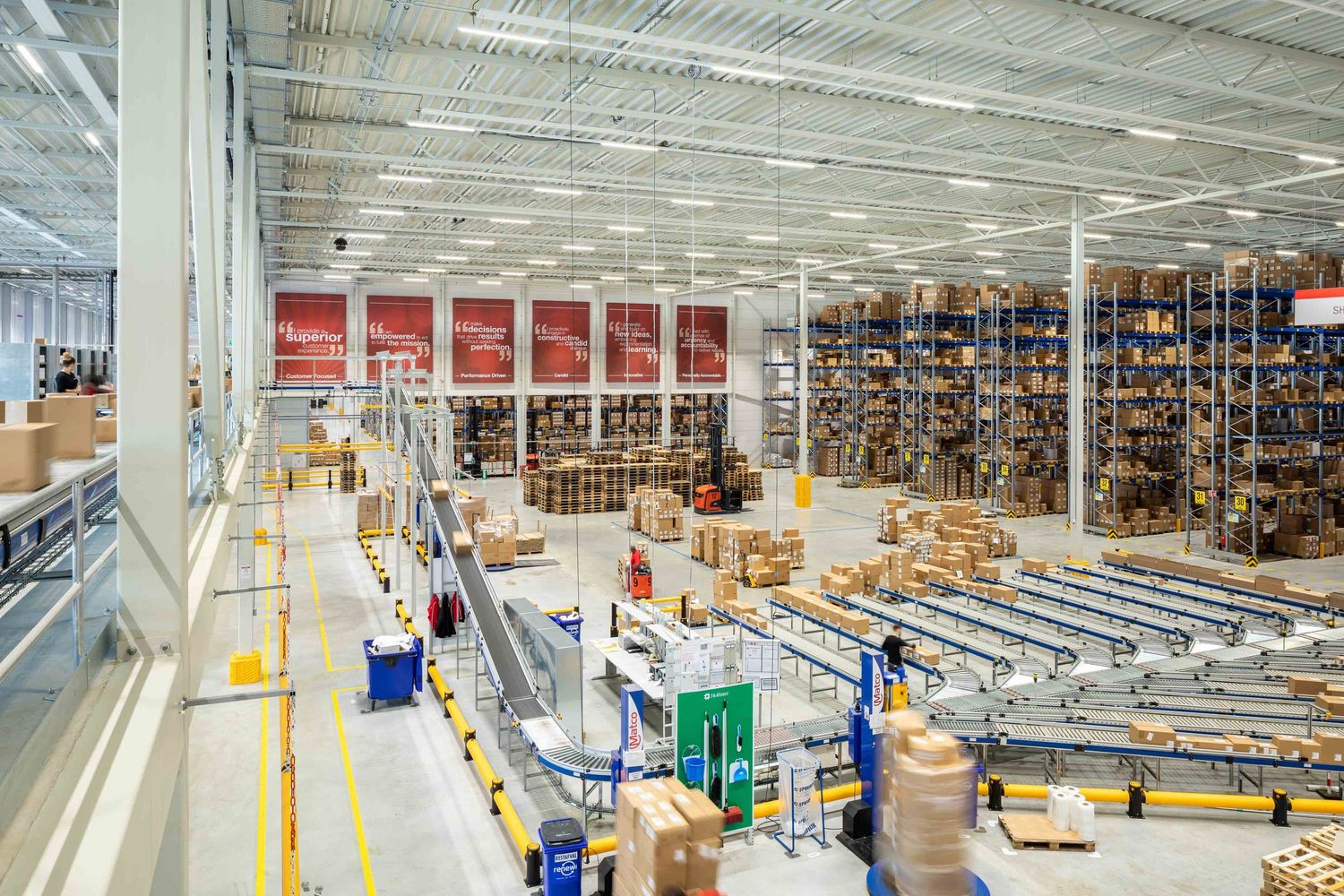 Large warehouse interior with conveyor belts and shelving systems storing boxes and inventory in an organized facility.