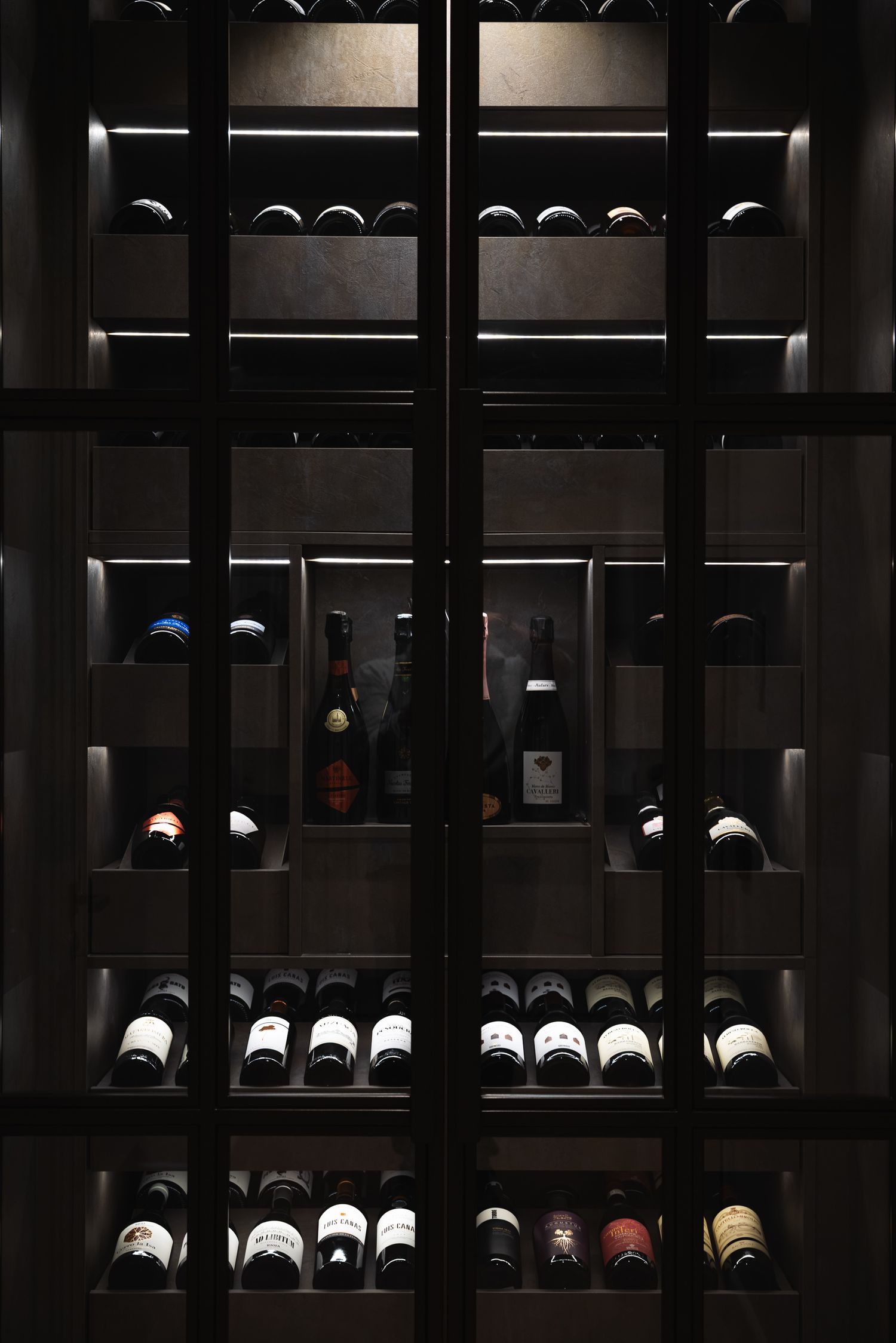 Dark wooden wine storage cabinet with glass doors displaying organized collection of wine bottles on multiple shelves.