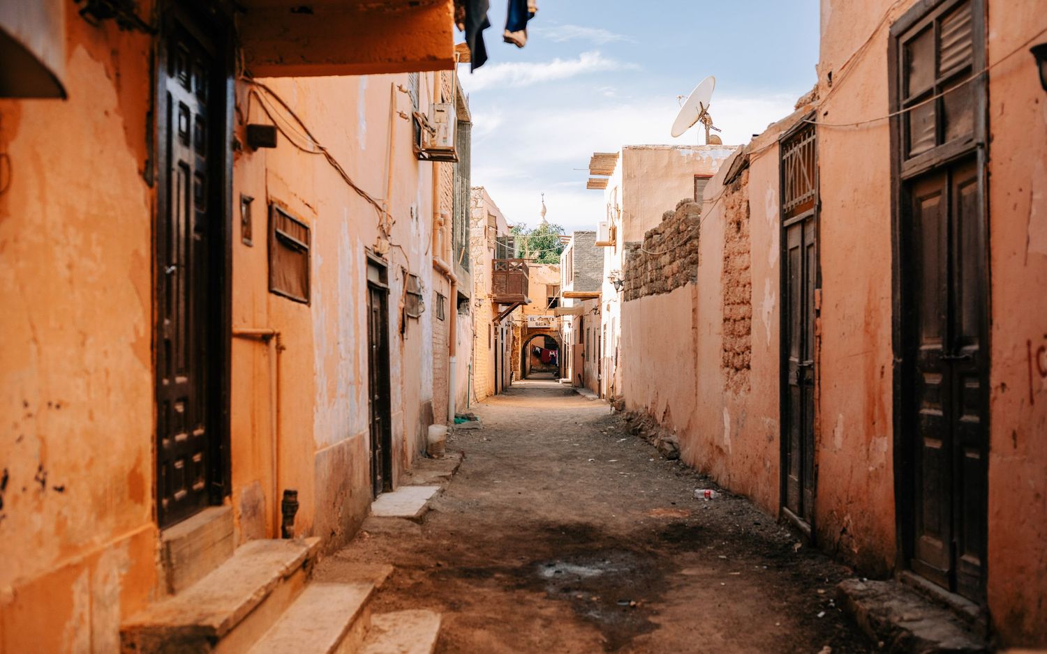Narrow alley with orange-tinted walls and traditional wooden doors in an old town.
