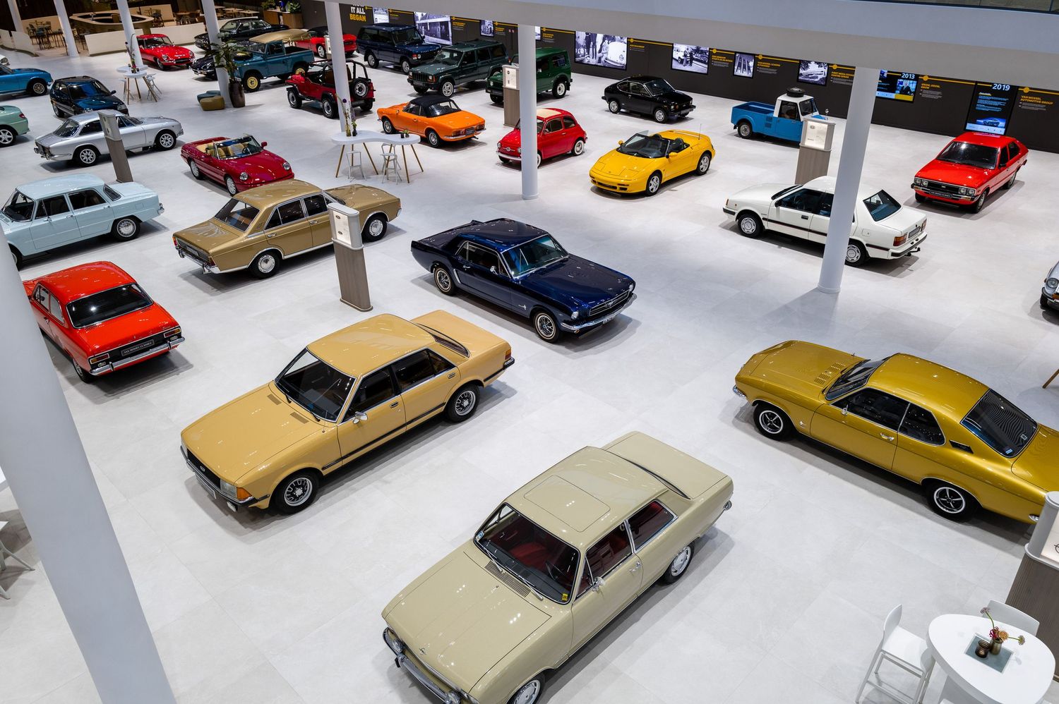 A collection of vintage toy cars and model vehicles arranged in neat rows on a white display surface.