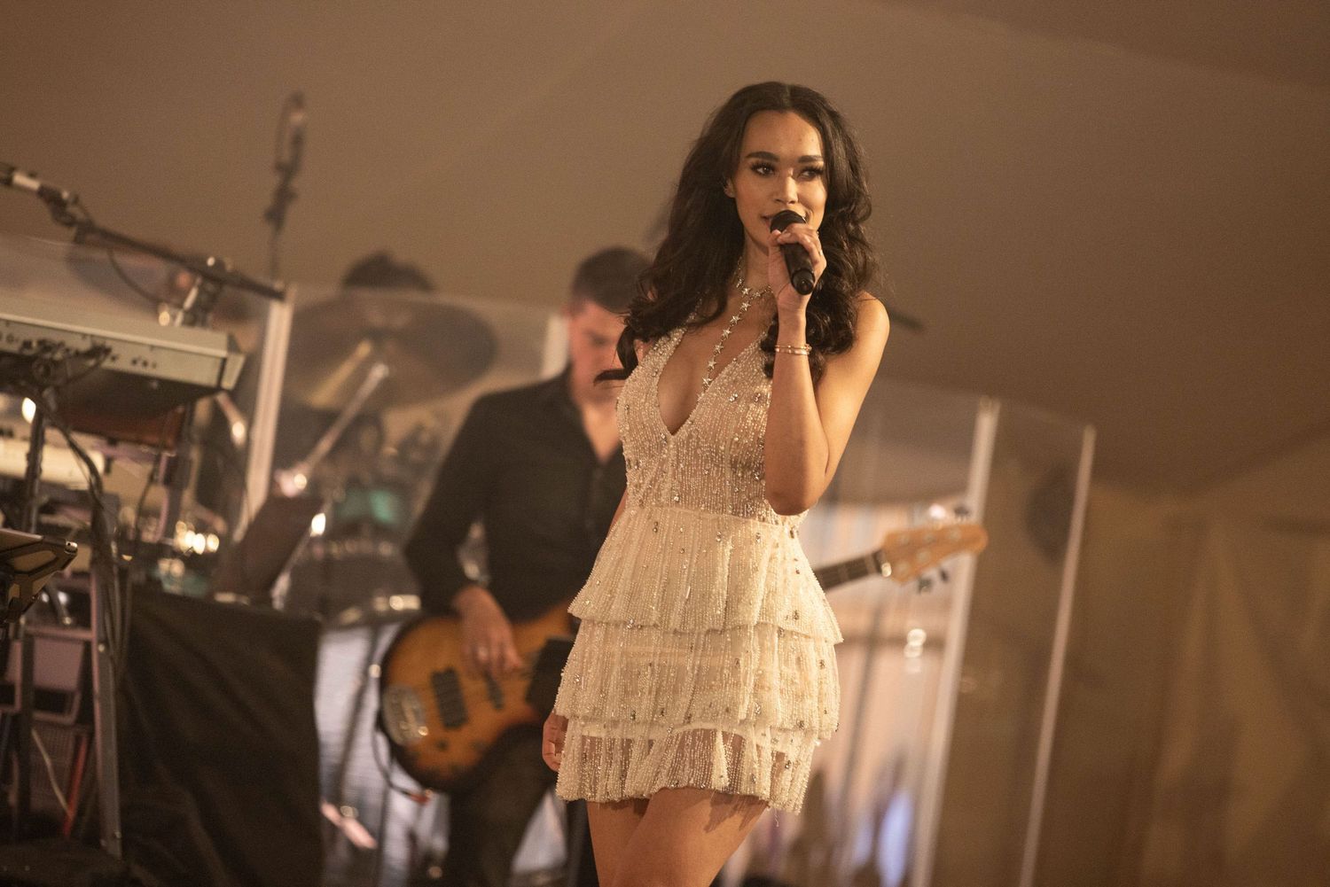 A performer in a white dress sings passionately on stage during a live concert performance.