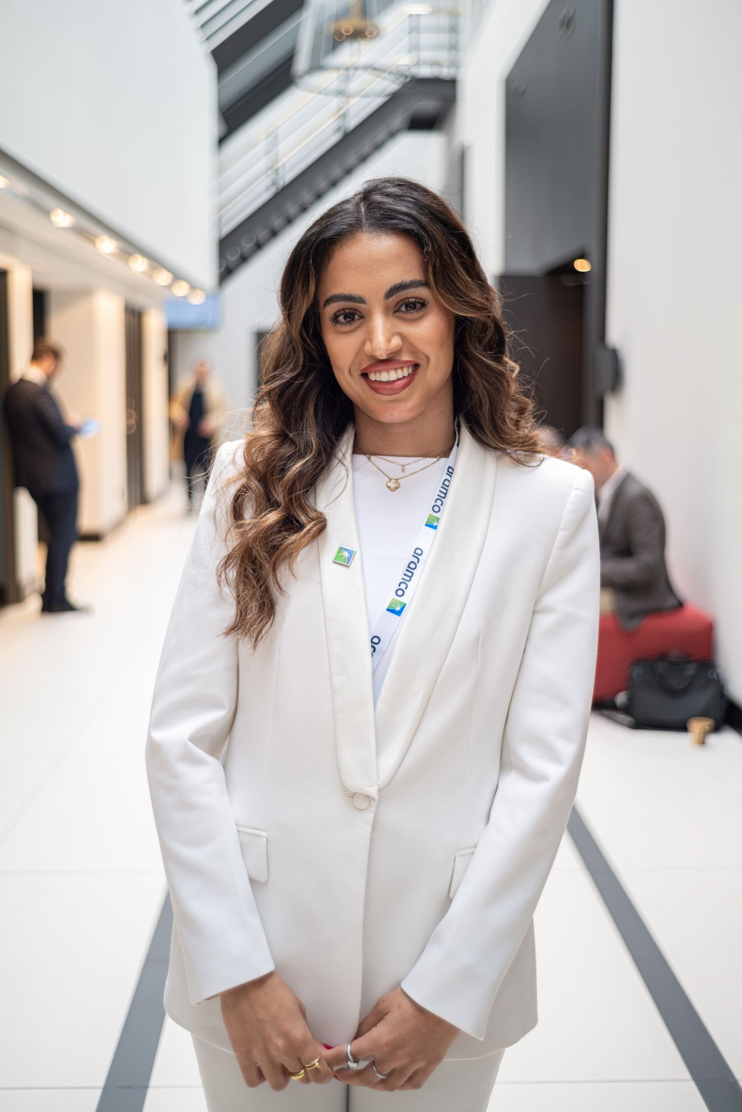 Professional in white blazer standing in modern office hallway.