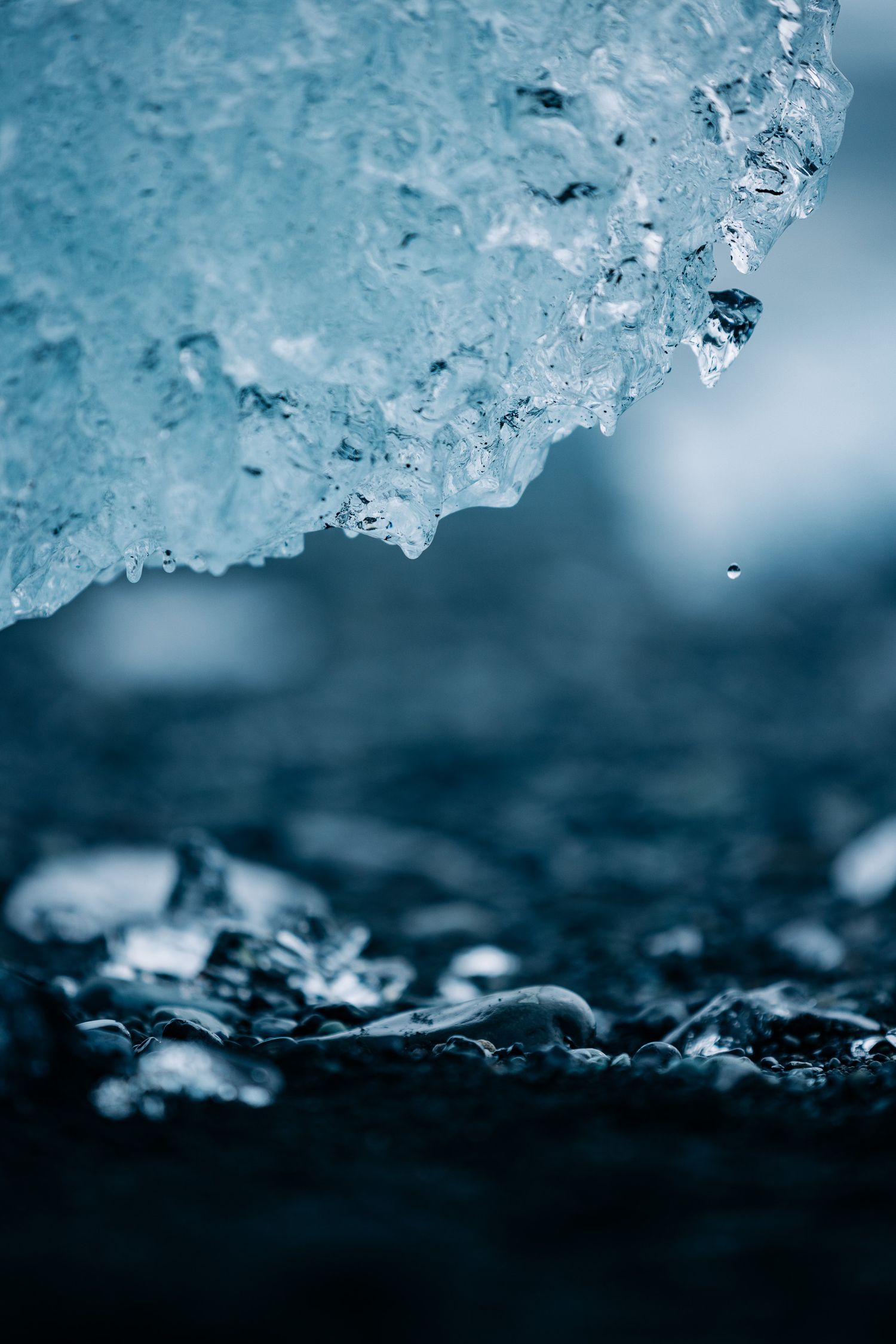 Close-up macro photography of melting ice crystals with a blue tinted background creating an abstract winter pattern.