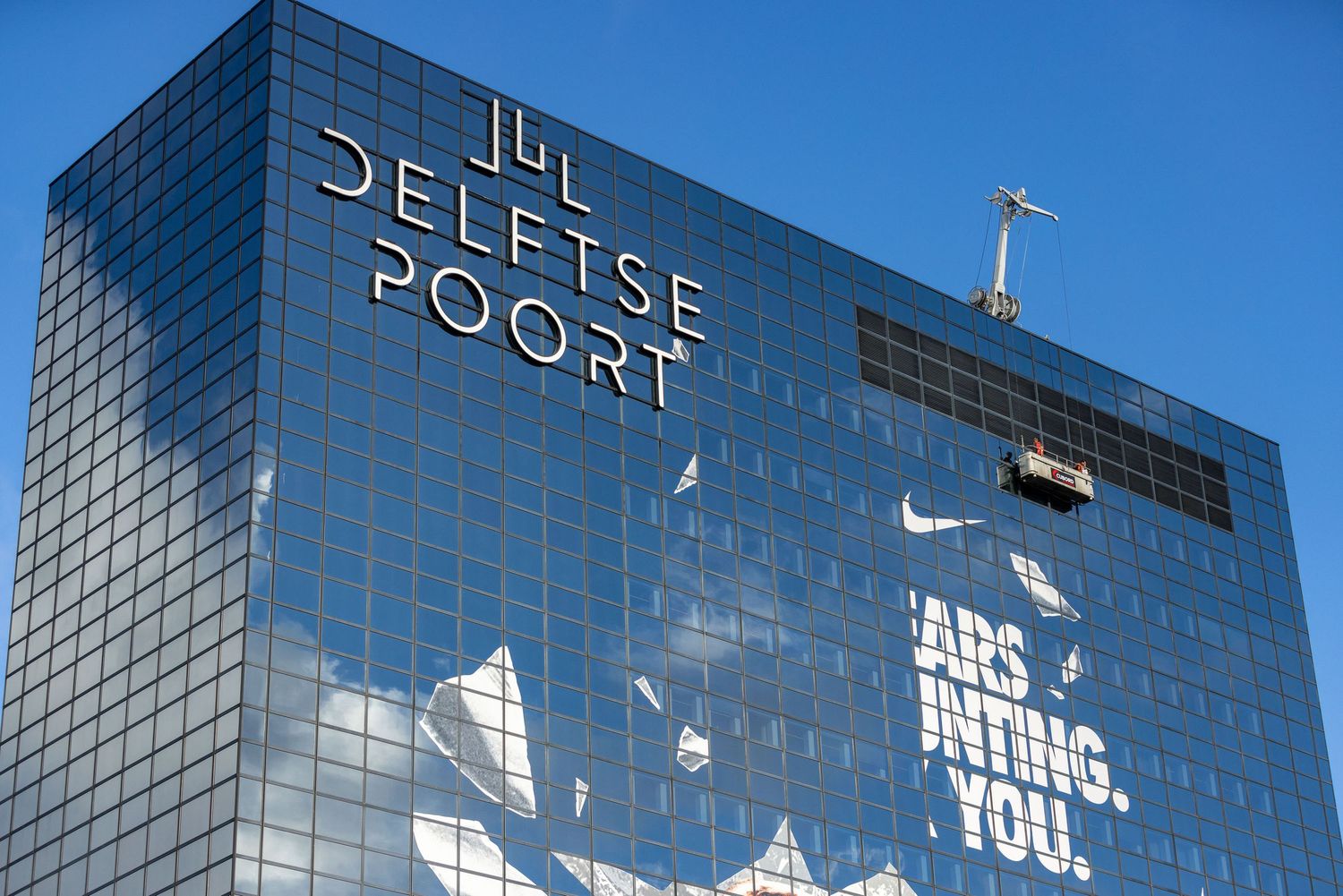 Delftse Poort skyscraper in Rotterdam with reflective glass facade and Nike advertisement under clear blue sky.