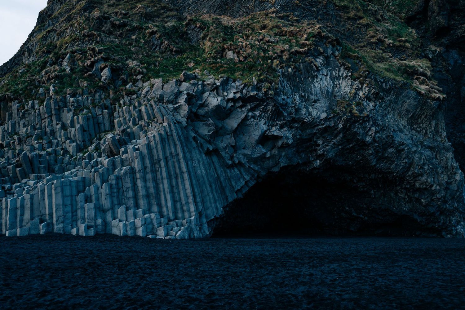 Dramatic basalt columns rise from the sea along a rugged coastline with dark cliffs and crashing waves.