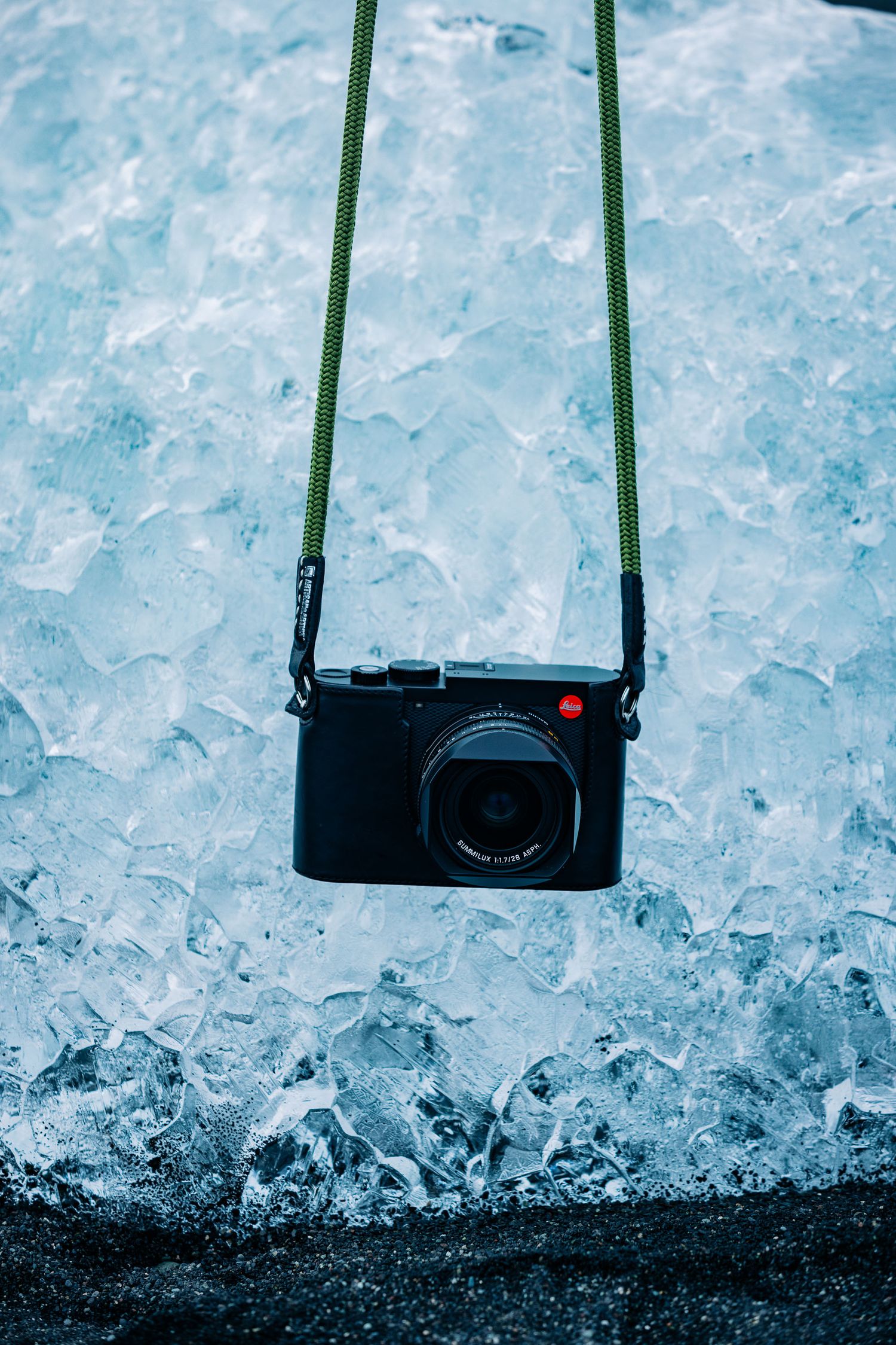 A black digital camera with green strap hangs against a backdrop of crushed ice and frost.