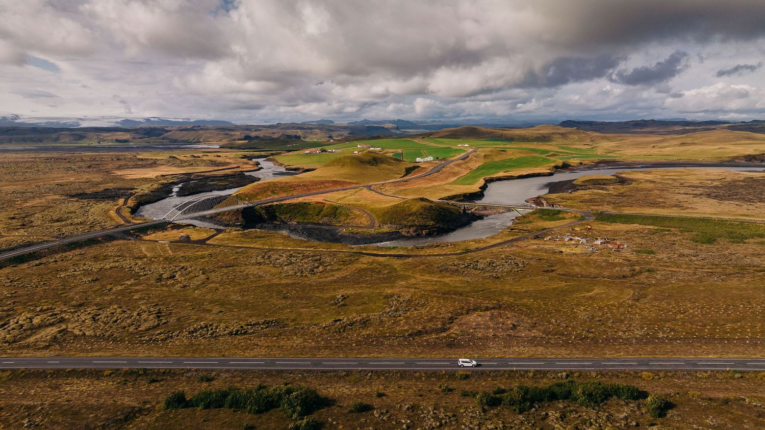 Dramatic panoramic landscape of rolling hills and winding roads under moody cloudy skies in rural countryside.