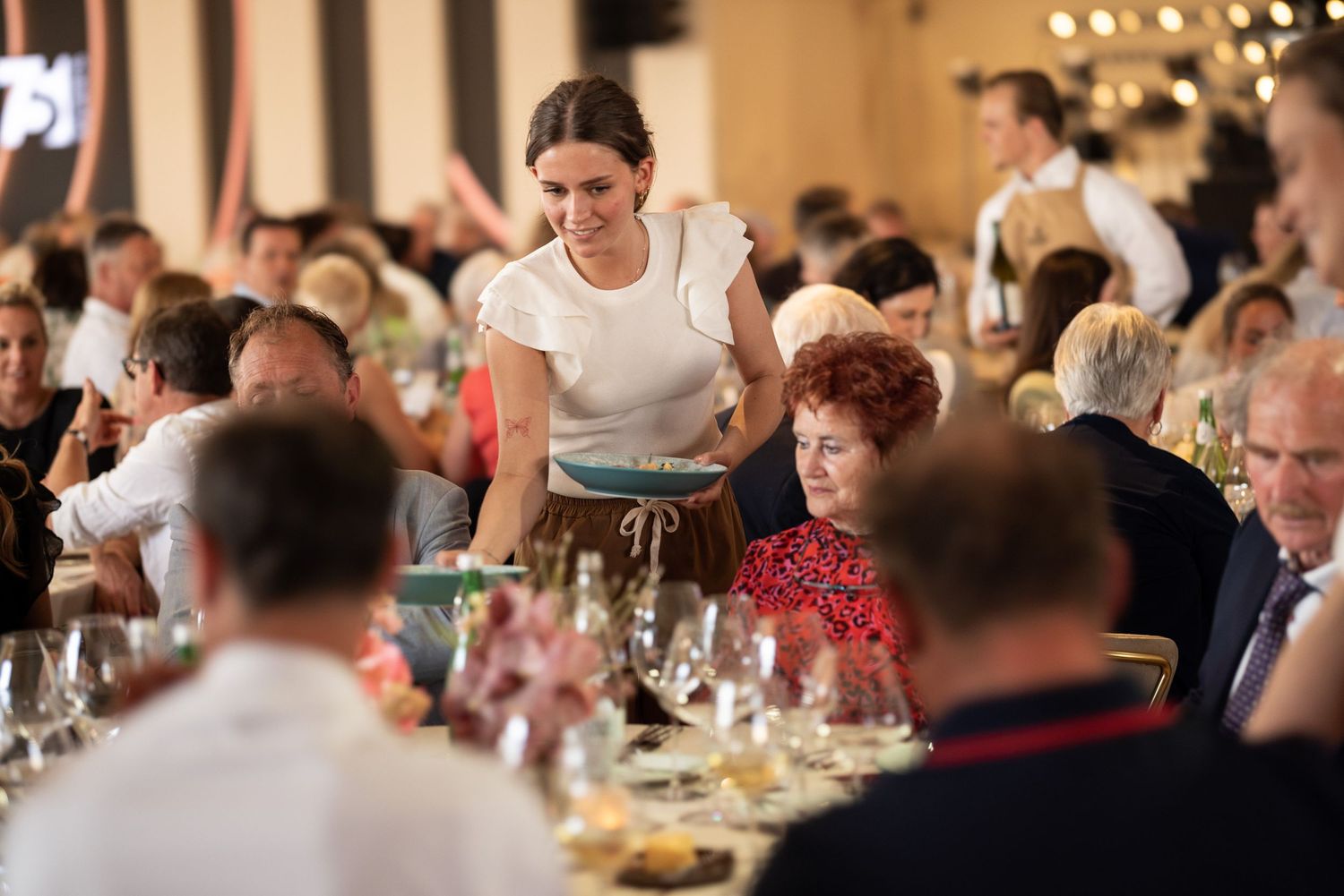 An indoor reception venue filled with dining guests at round tables during an evening event.