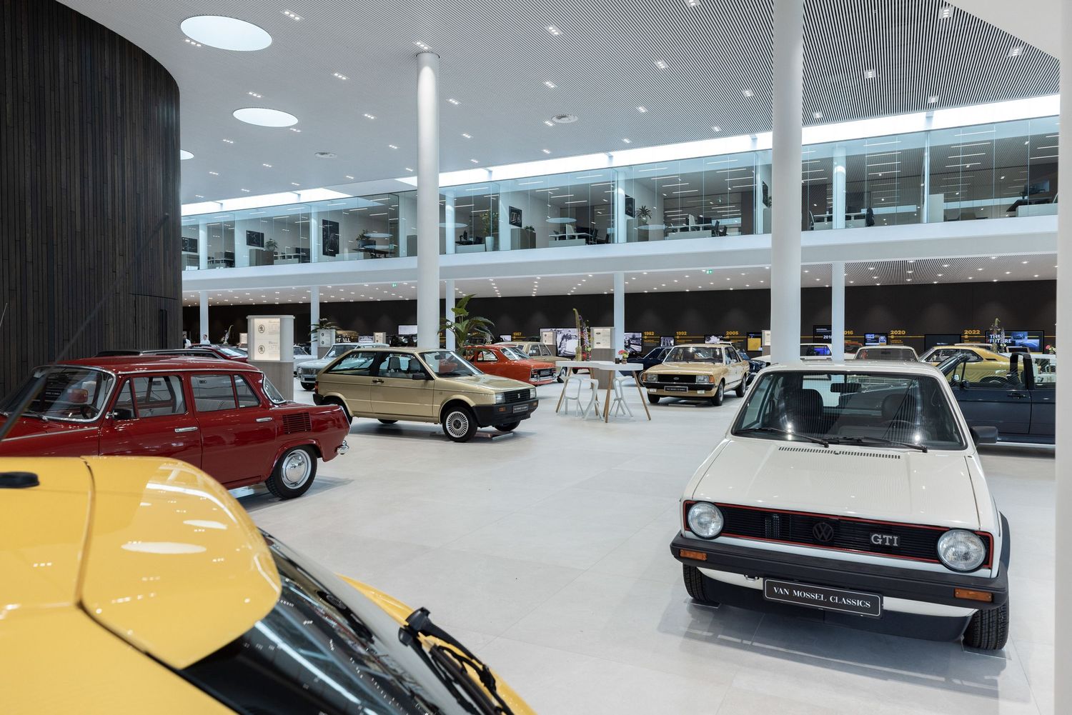 Modern car dealership interior with bright lighting and classic vehicles arranged on white flooring.