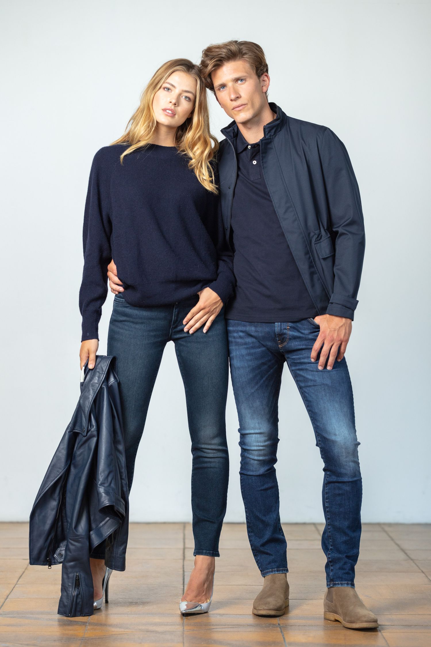 Stylish couple in coordinating navy and denim outfits posing together against white background.