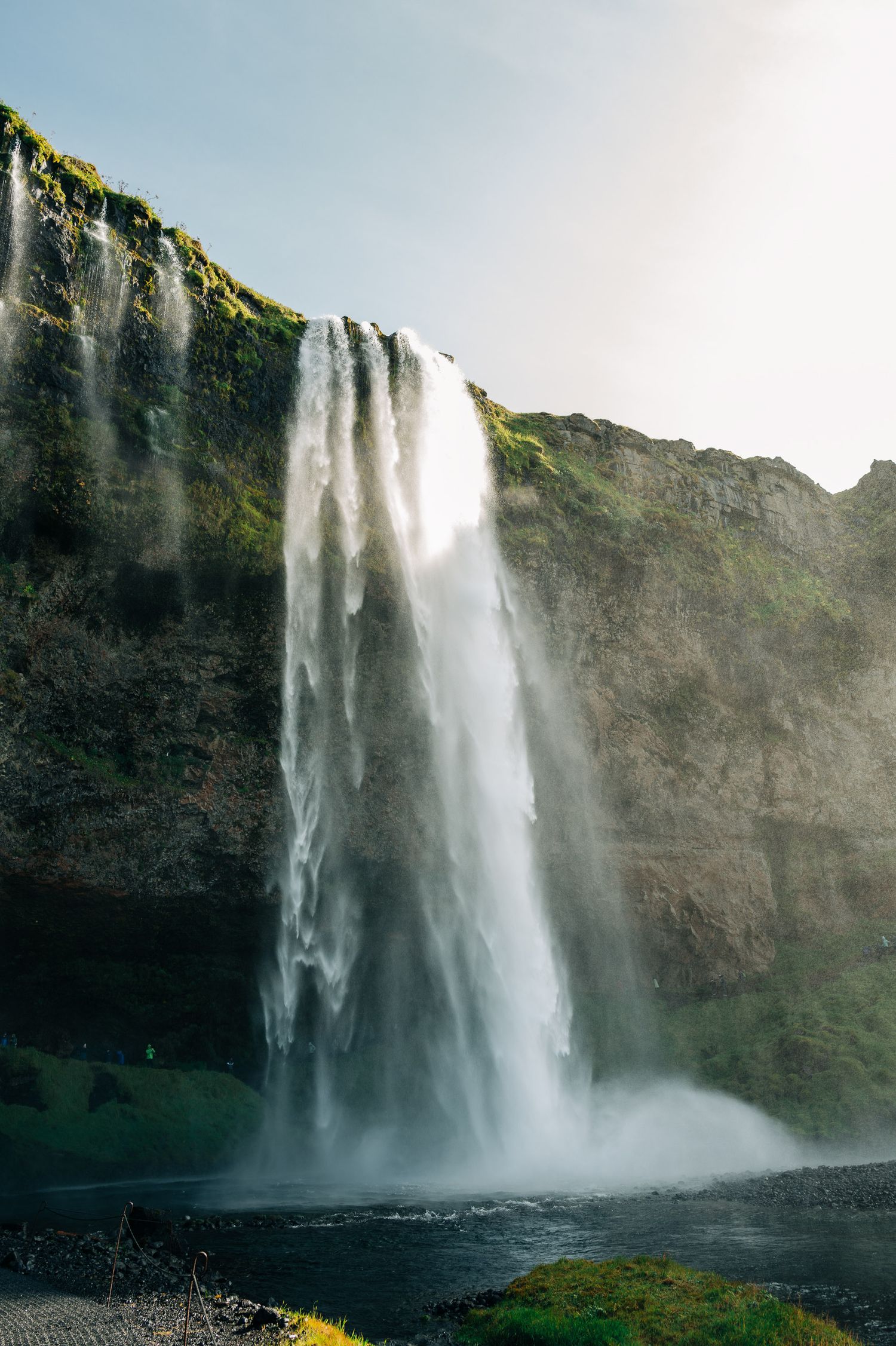 Powerful waterfall plunges down dark rocky cliffs creating mist in the sunlight.