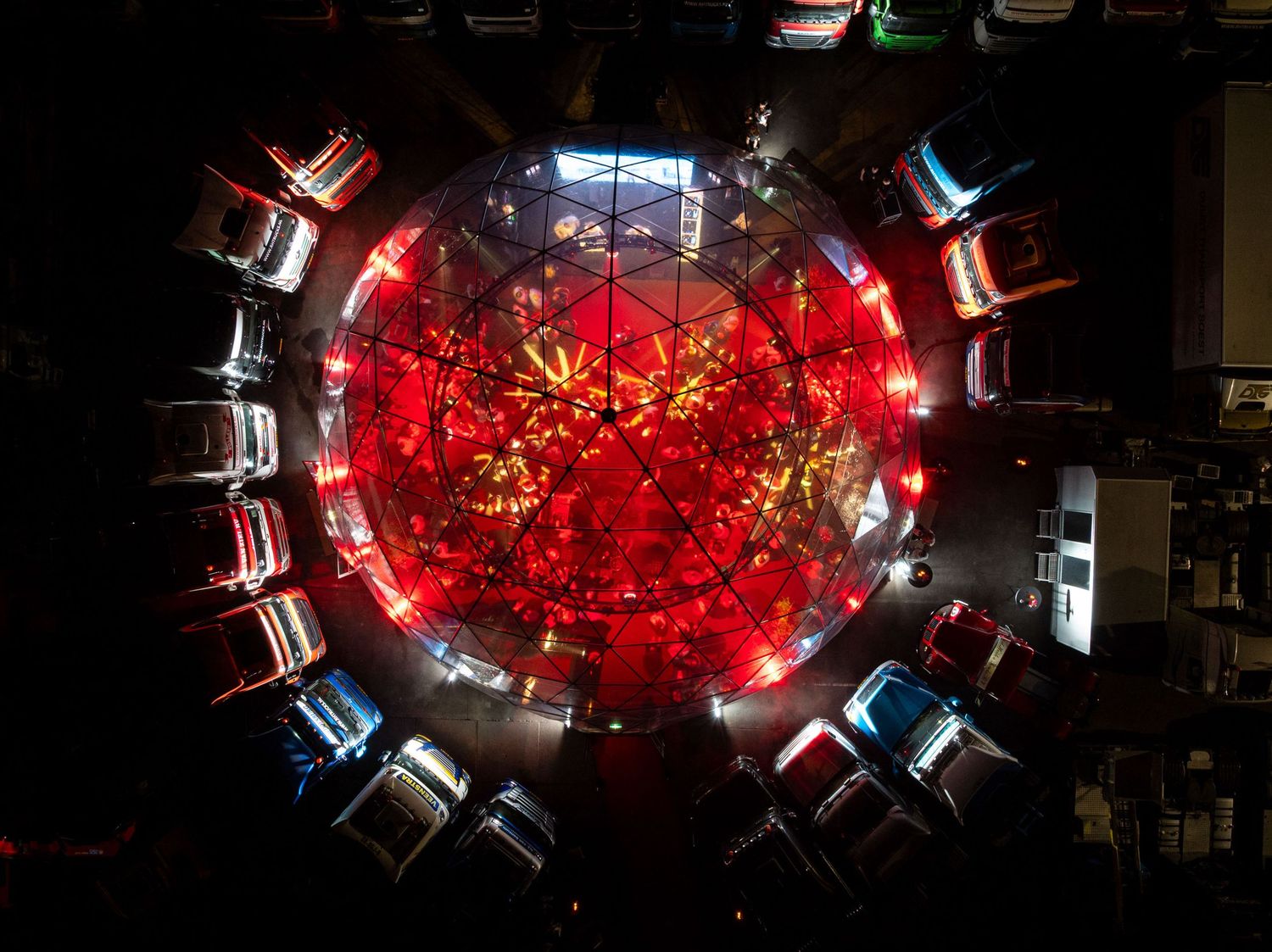 Aerial view of cars arranged in a circle around a glowing red light installation at night.