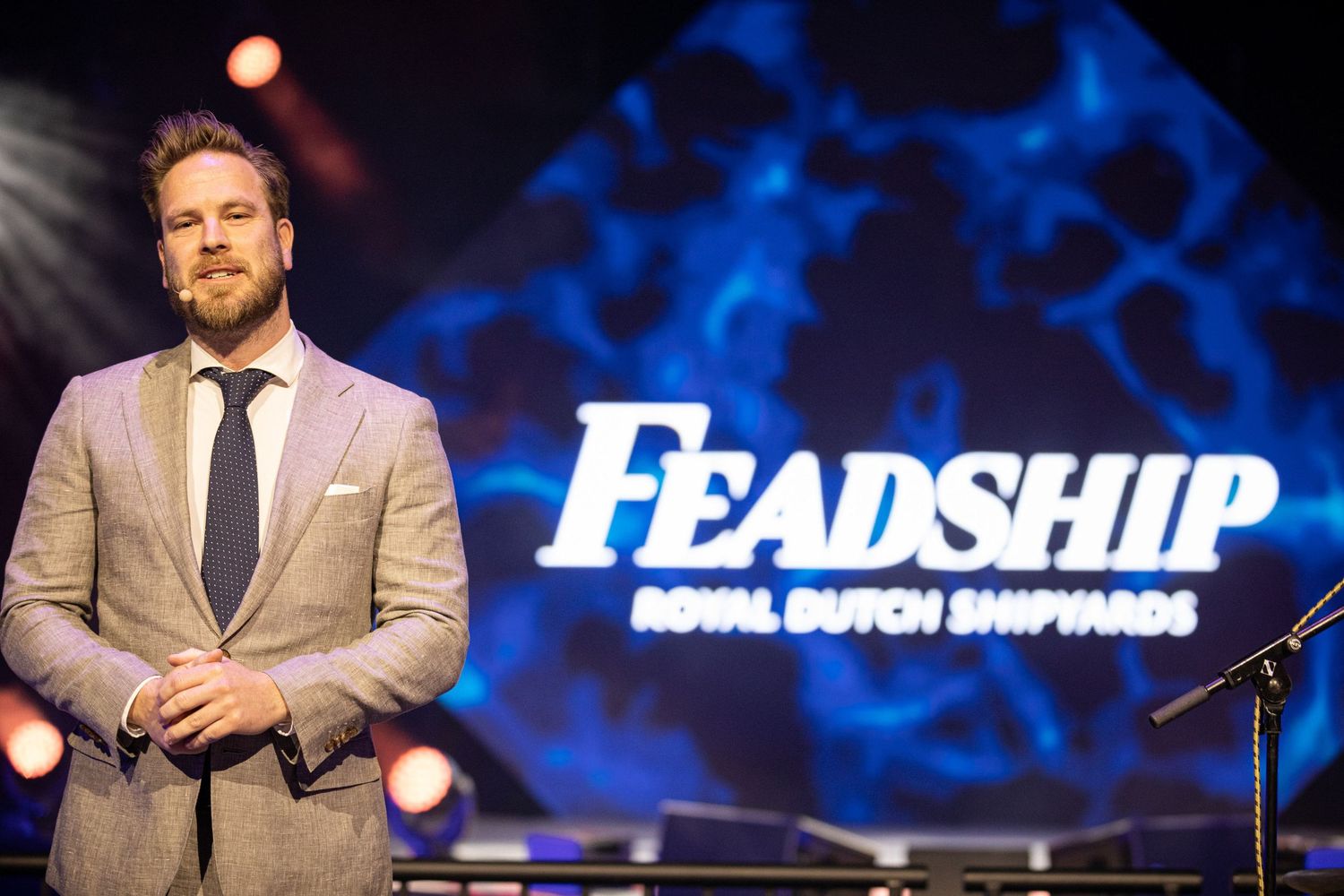 Speaker presents on stage at leadership conference with blue illuminated backdrop and podium.