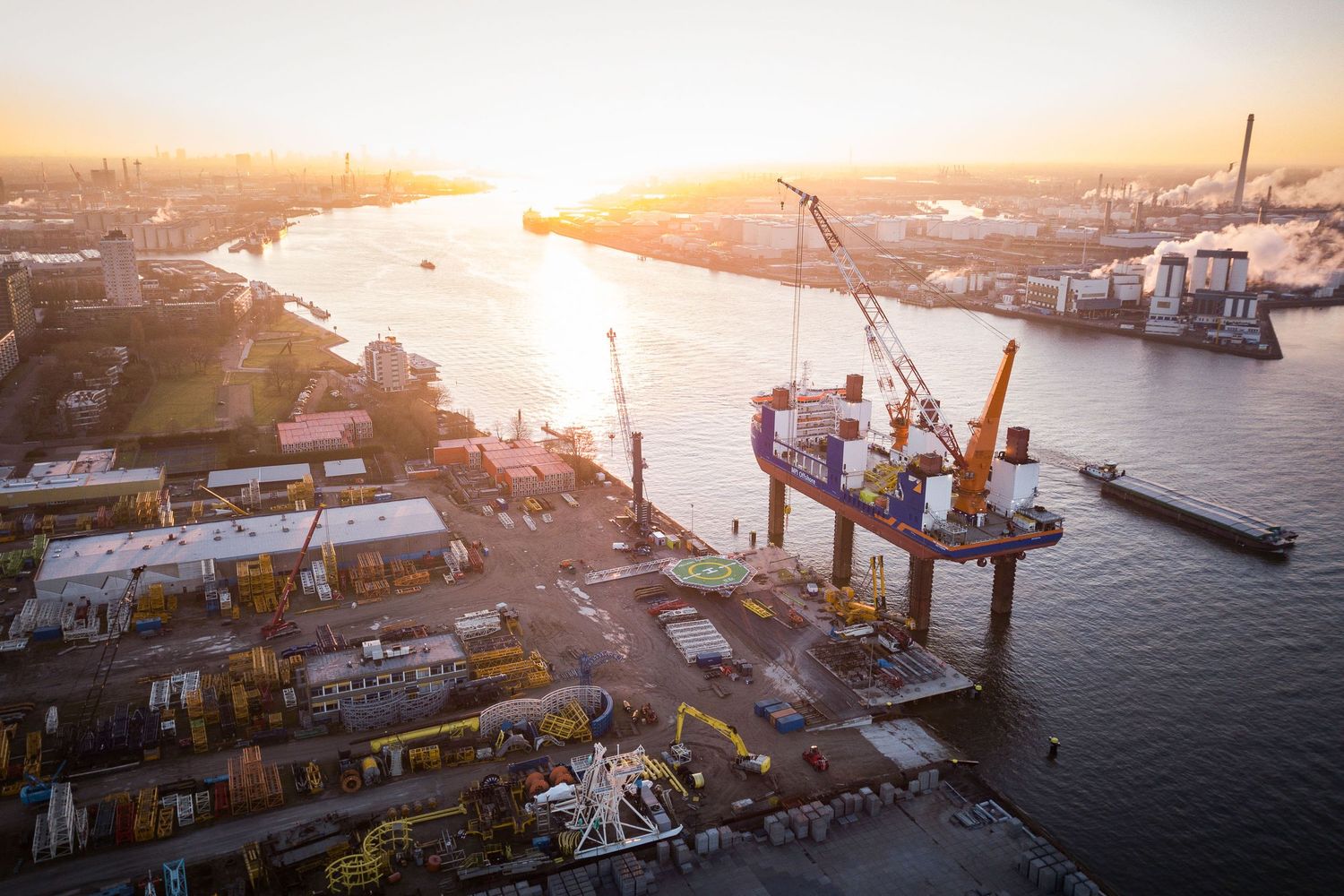 Aerial view of port terminal with cargo cranes silhouetted against golden sunset.