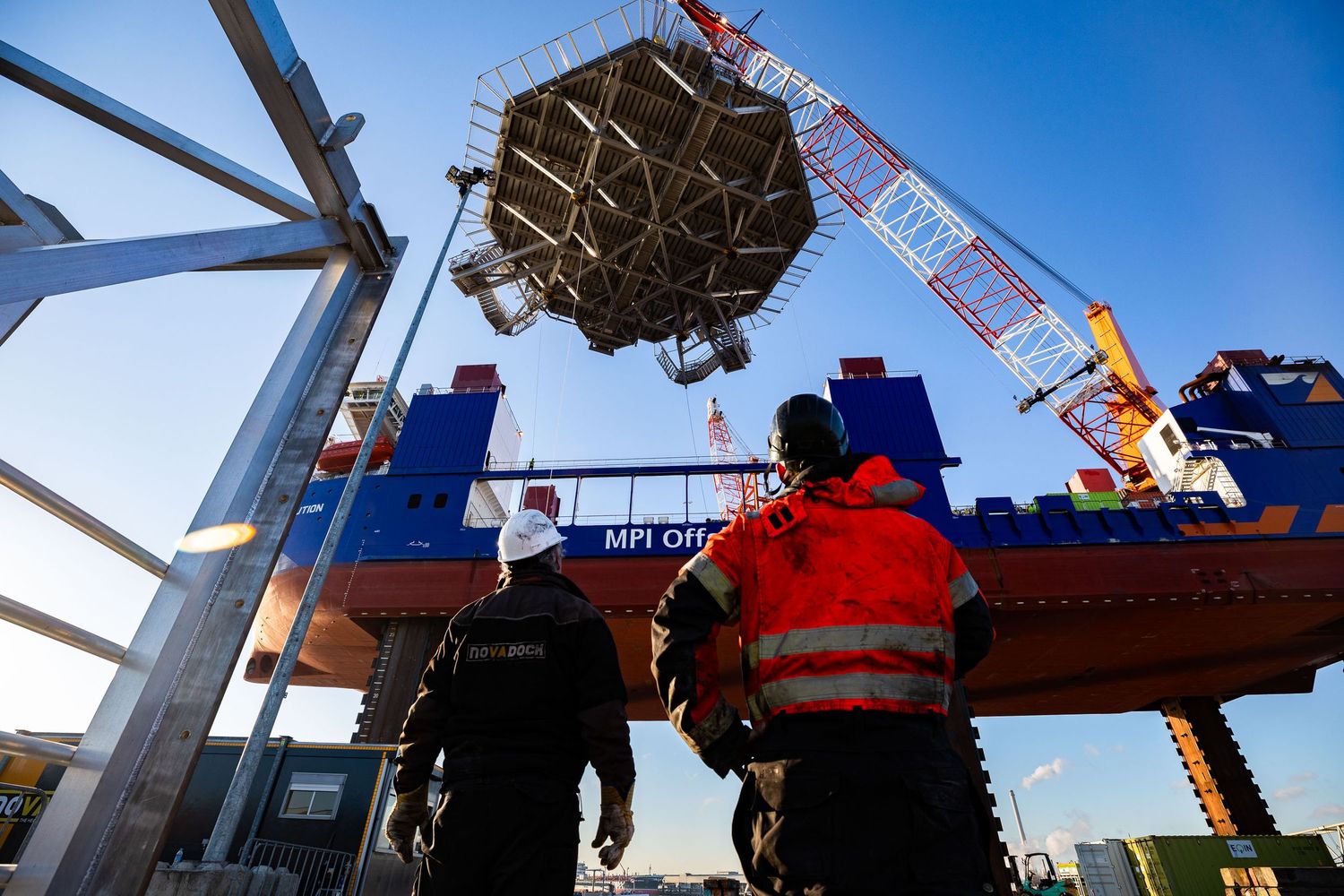 Workers observing heavy machinery operations at an industrial construction site.
