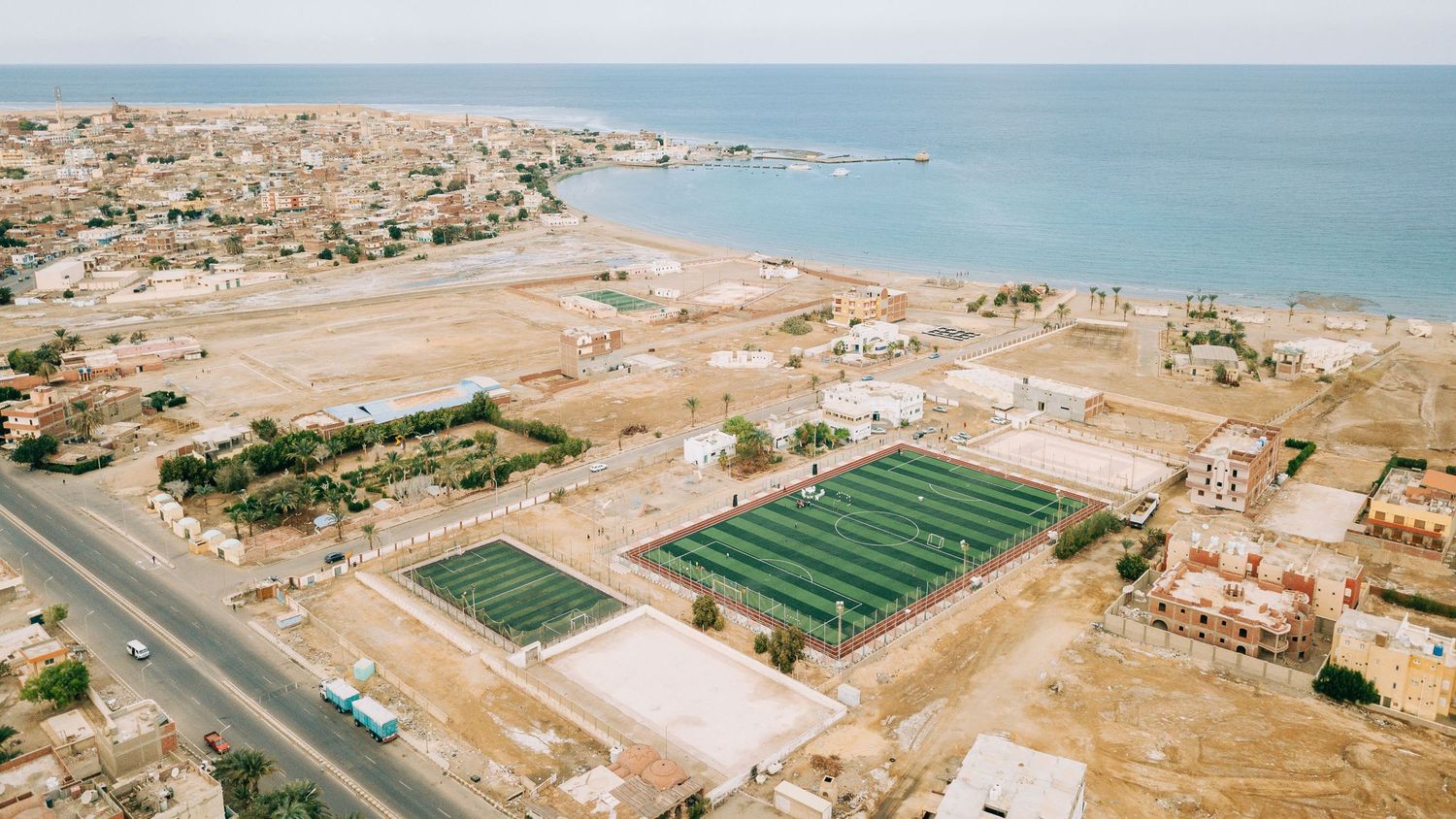 Panoramic aerial view of coastal city with sports fields and buildings along the shoreline.