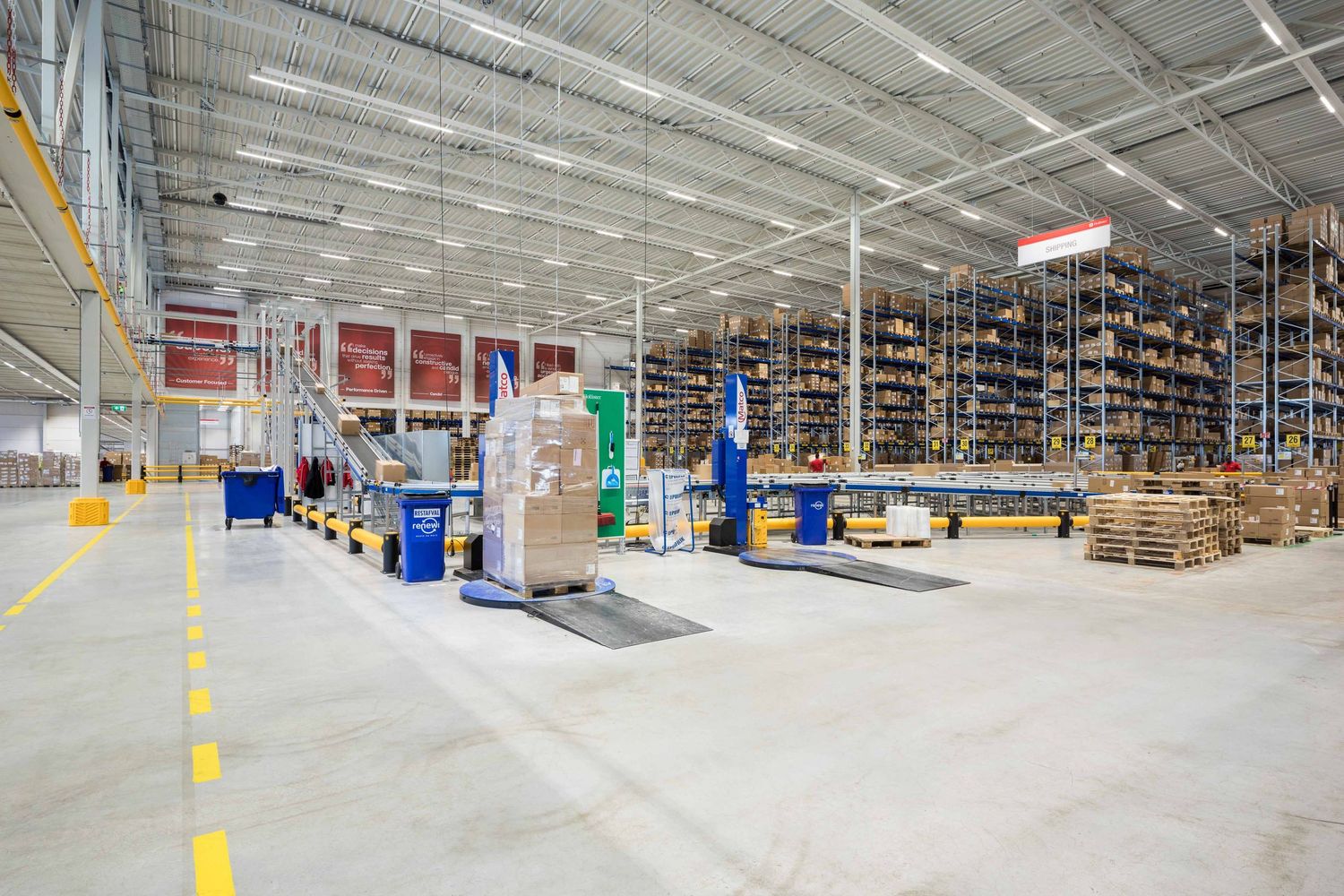 Large distribution warehouse interior with tall storage racks, yellow support beams, and concrete floors stretching into distance.