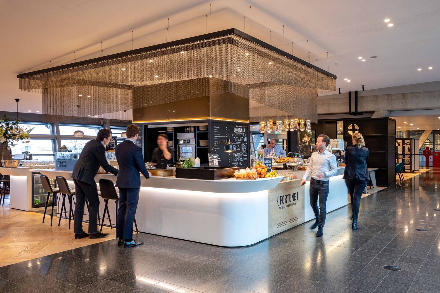 Modern office lobby with white marble counters, recessed lighting, and people walking through the open space.