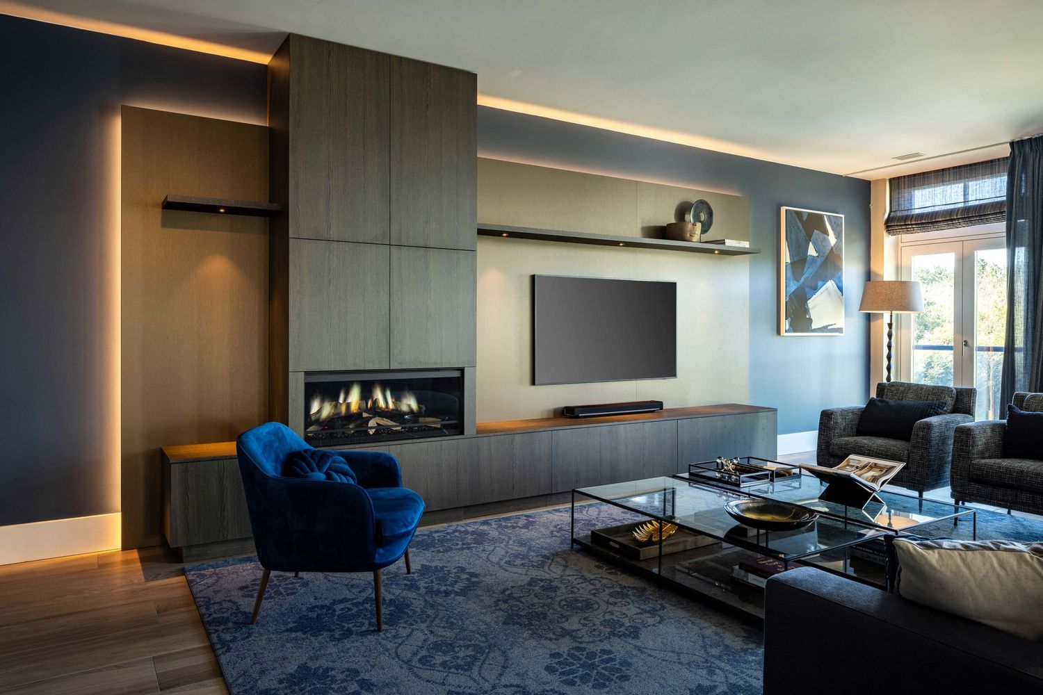 Modern apartment interior with dark walls features sleek built-in storage and blue accent chairs in natural lighting.
