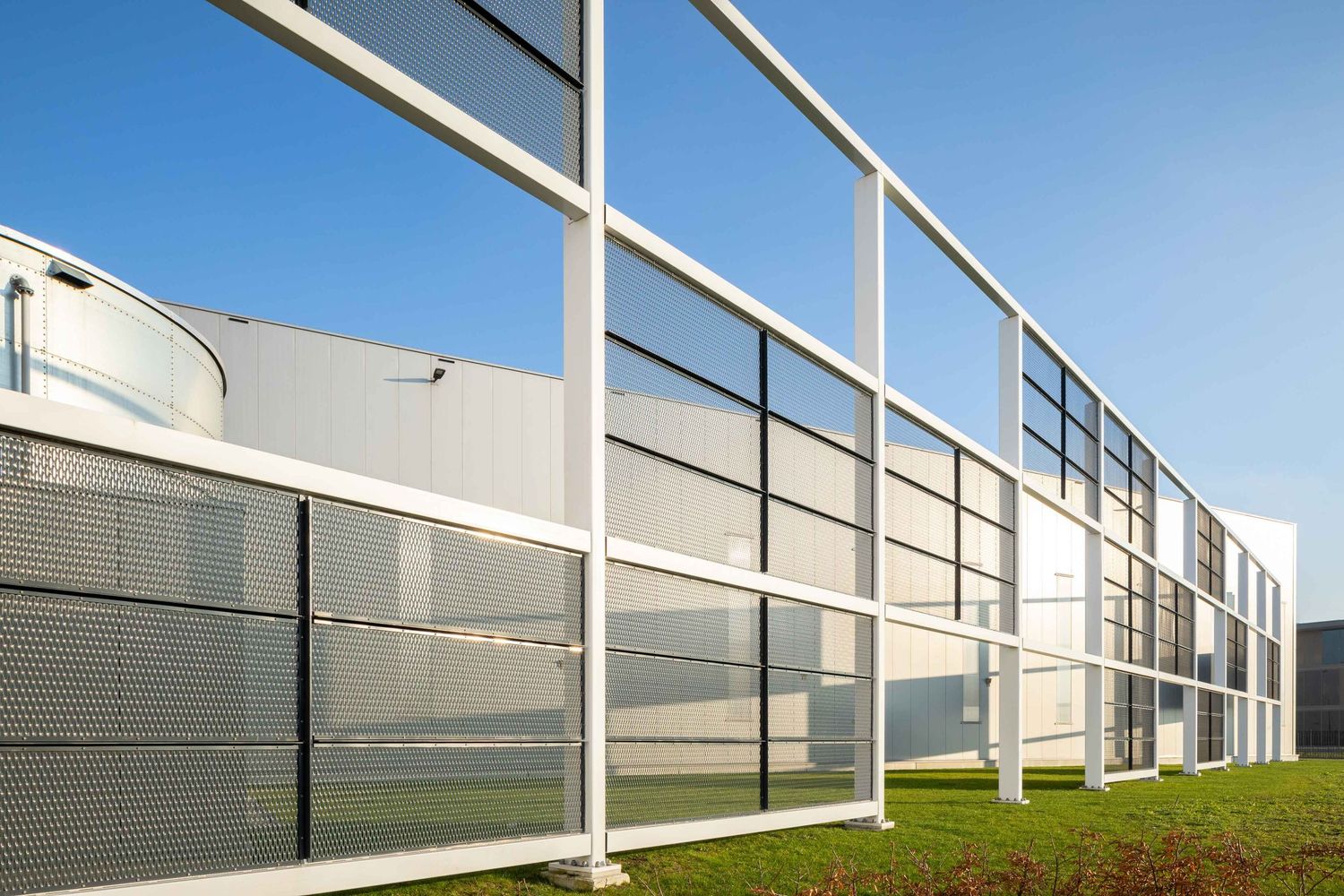 Modern white industrial building exterior with geometric metal framework against blue sky.
