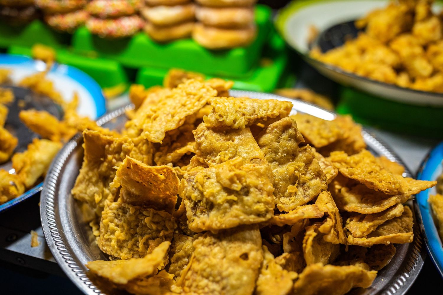 Golden-brown crispy snacks and crackers displayed on silver platters at a market stall.