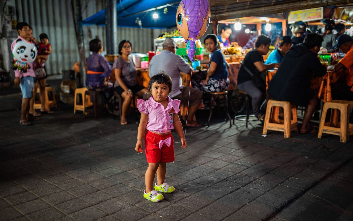 Lively night market scene with vendors and customers browsing under bright lights.
