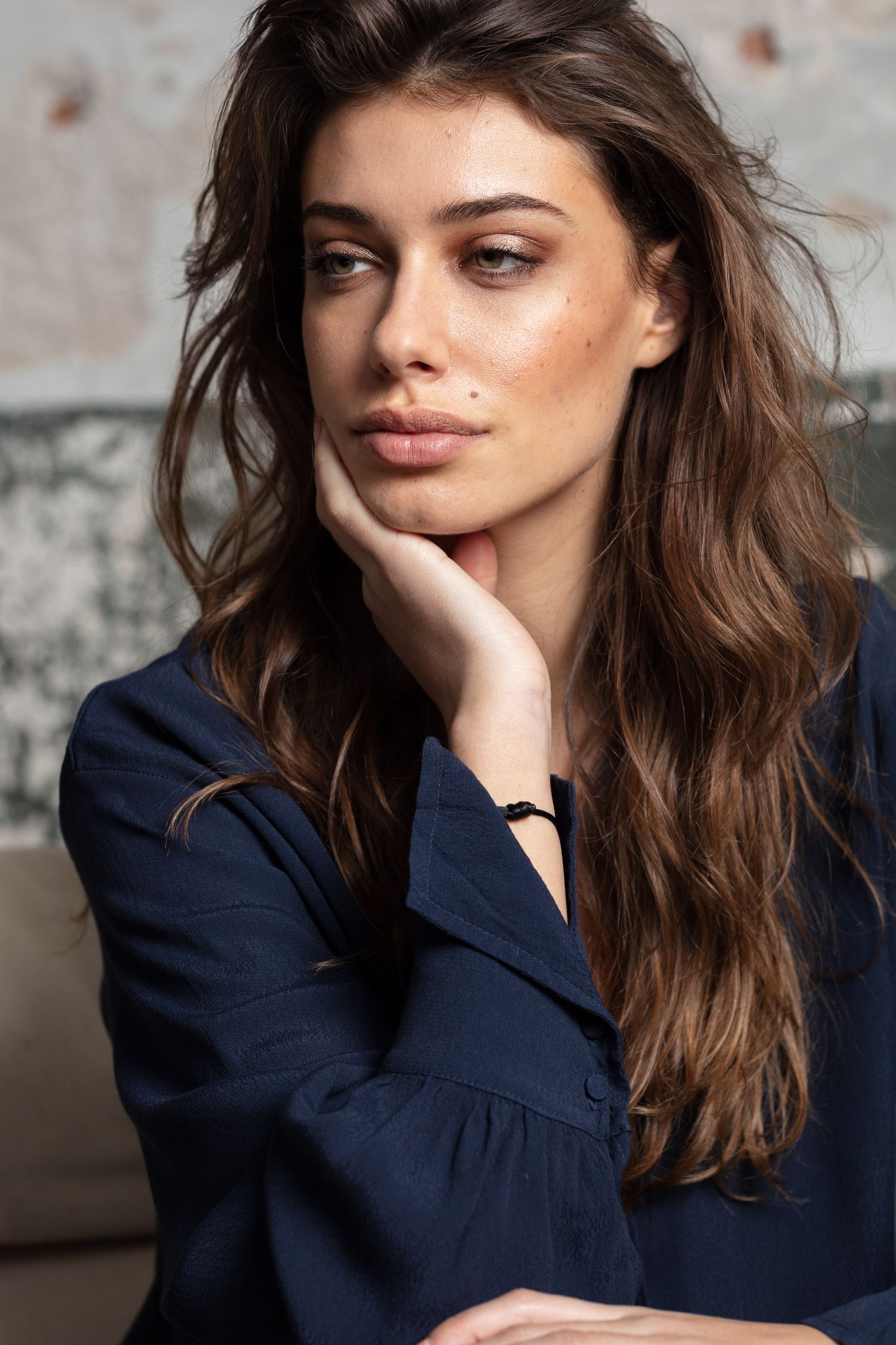 Moody portrait series in navy top against weathered brick wall background.