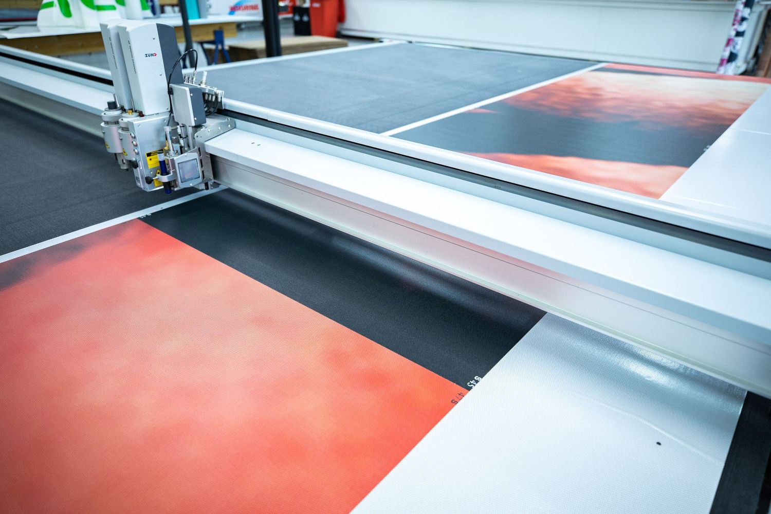Large format flatbed cutting machine processing colorful red and black vinyl sheets in a print production facility.