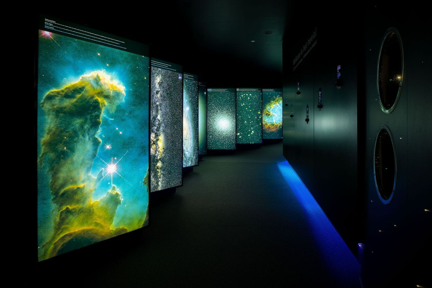 Dark corridor displaying illuminated NASA Hubble Space Telescope nebula photographs on gallery walls with blue accent lighting.