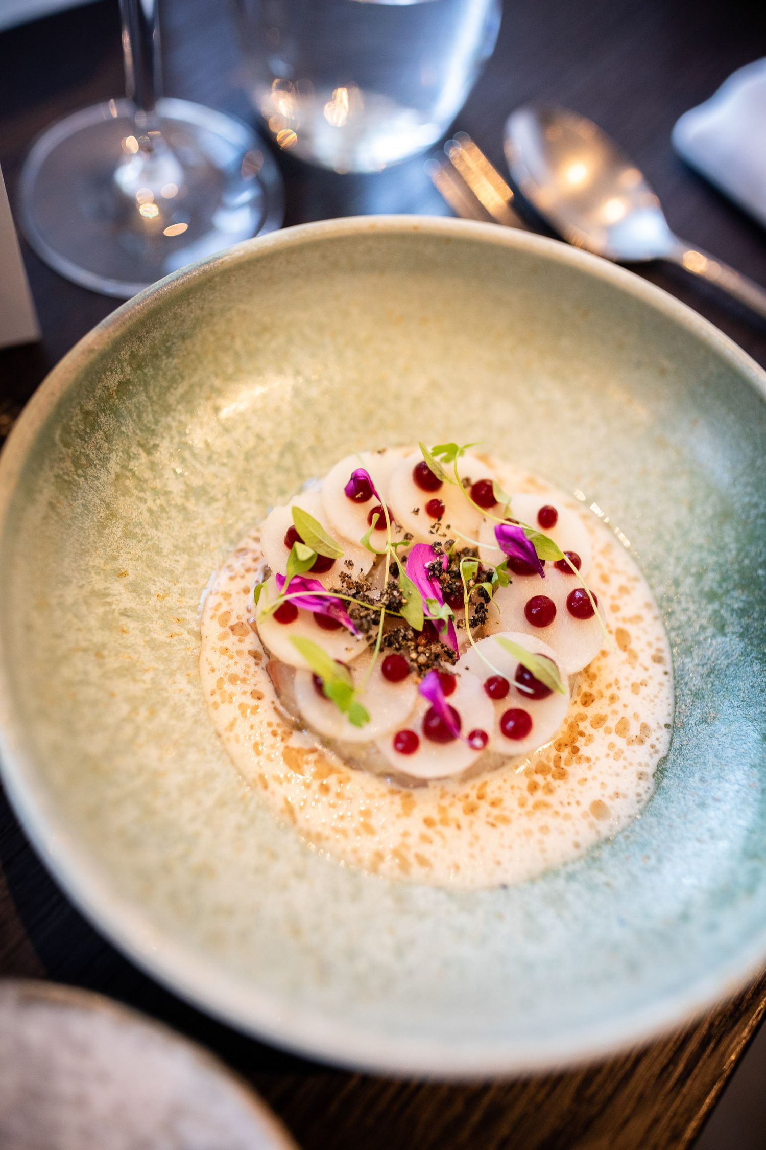 Elegant plated dessert with pomegranate seeds, purple edible flowers and microgreens on a textured blue ceramic bowl.