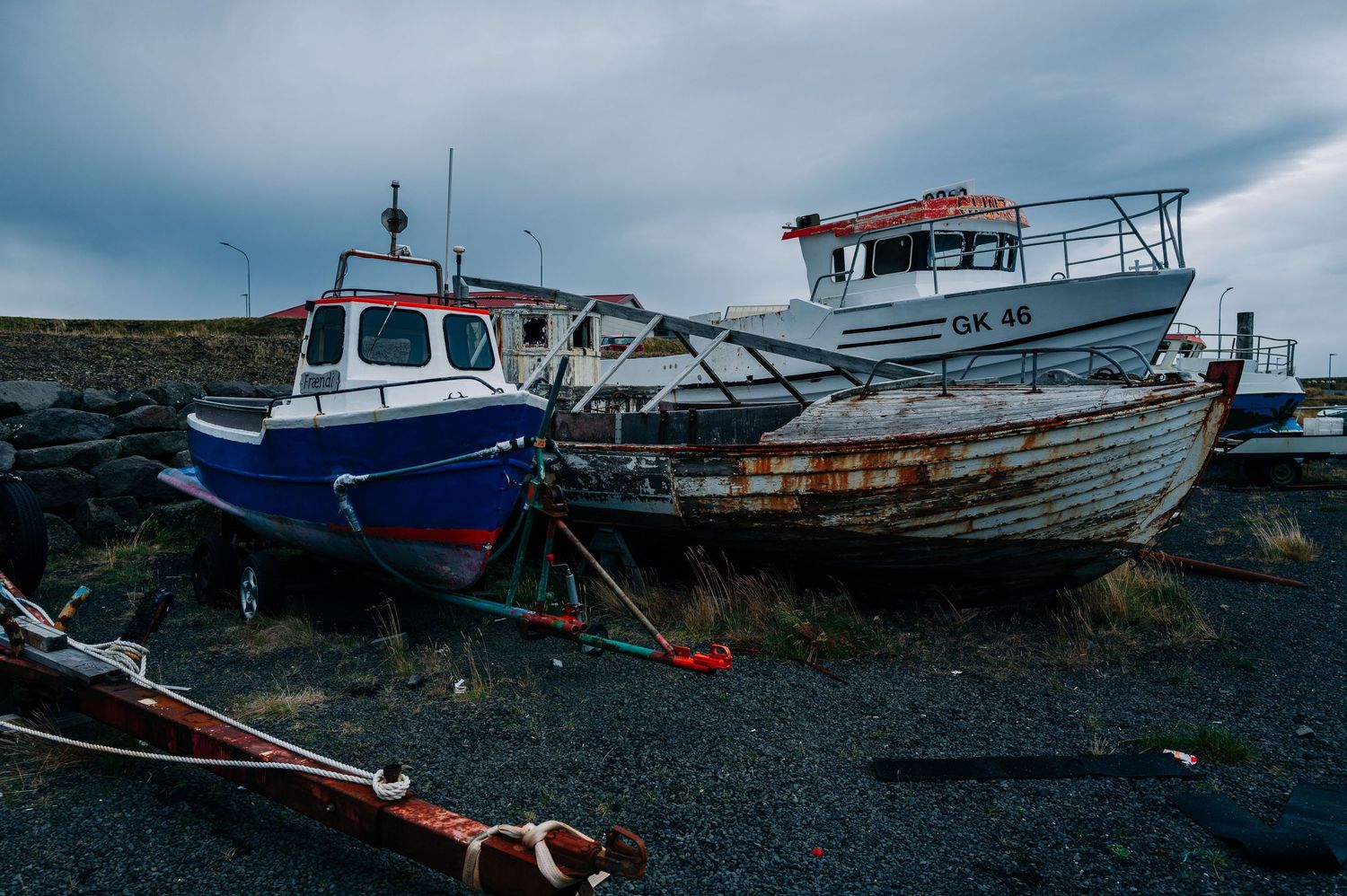 Abandoned wooden fishing boats rest on a rocky beach under moody gray skies.