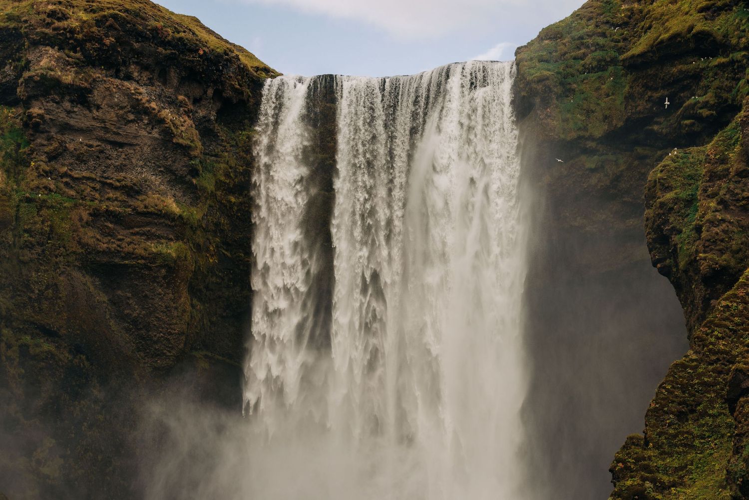Powerful Skogafoss waterfall cascades down moss-covered cliffs in Iceland, creating misty spray in the air.