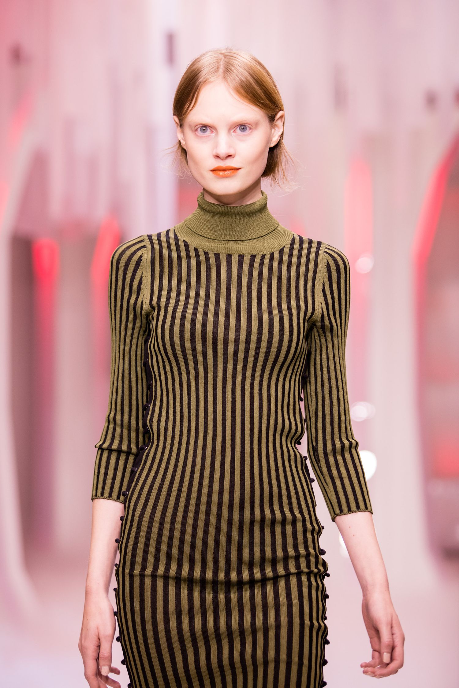 Model walks runway in olive green and black striped turtleneck dress with 3/4 sleeves at fashion show.