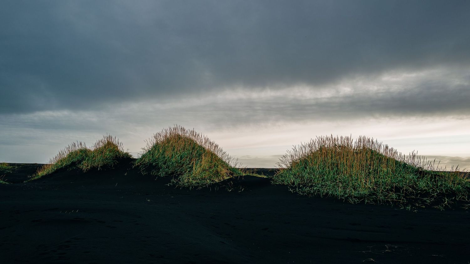 A panoramic view of a dramatic stormy sky with dark clouds rolling over a green hillside at dusk.