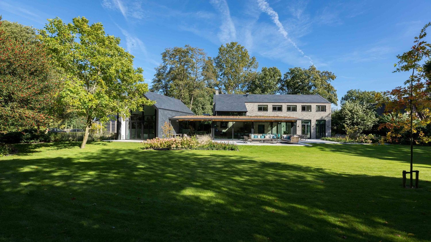 A panoramic view of a lush green lawn with mature trees and a white building visible in the distance.