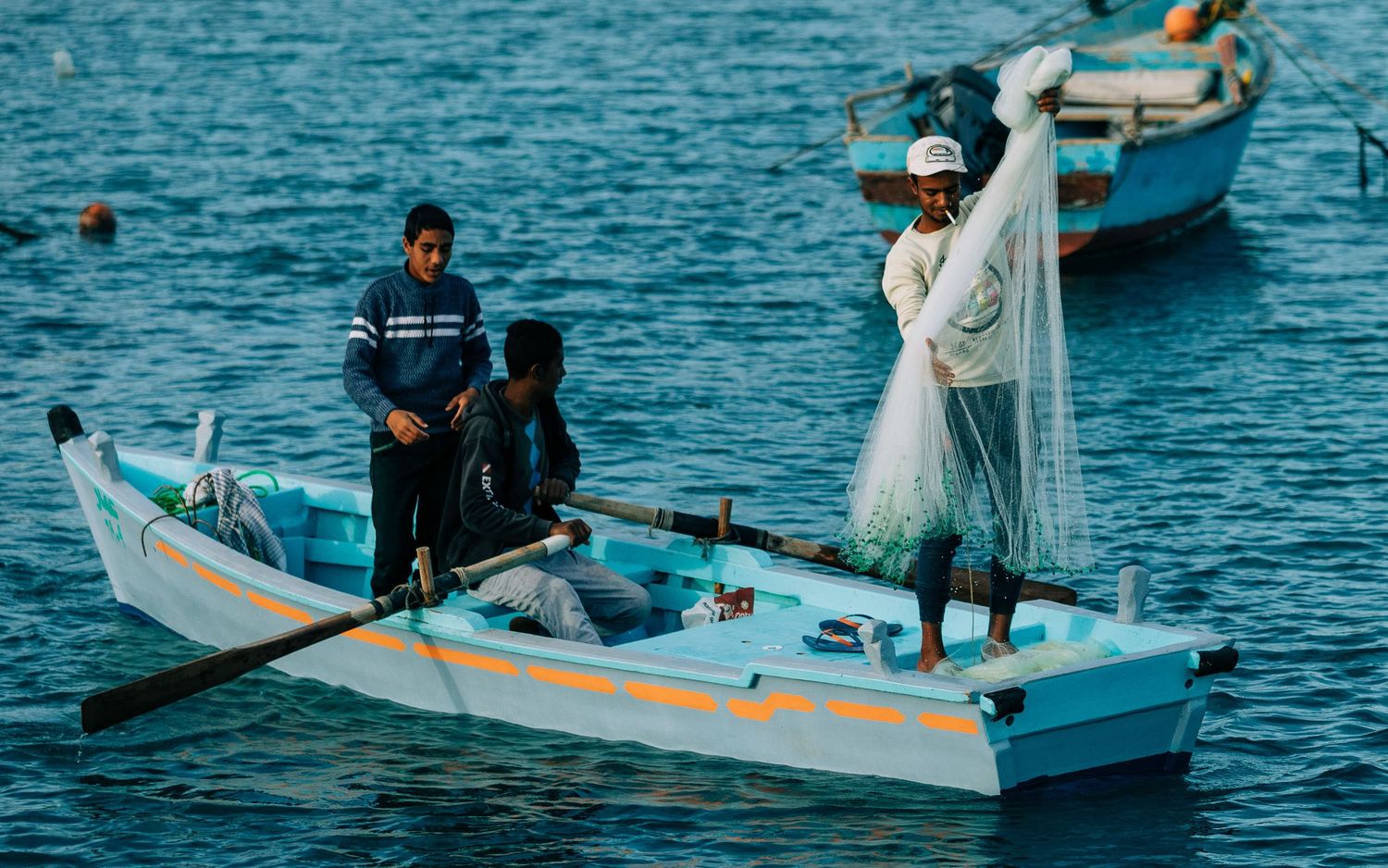 Small boats float on bright turquoise waters with fishing nets being cast from their sides.