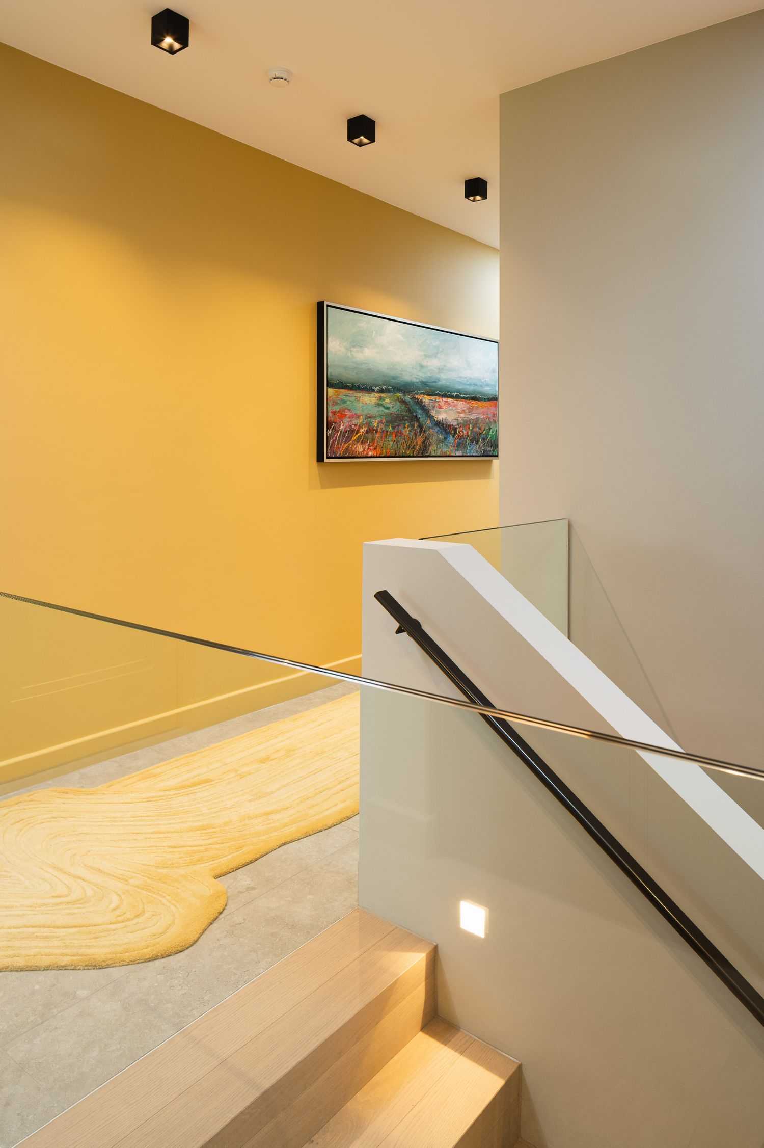Modern staircase interior with black handrail and warm lighting casting geometric shadows on white walls and wooden floor.