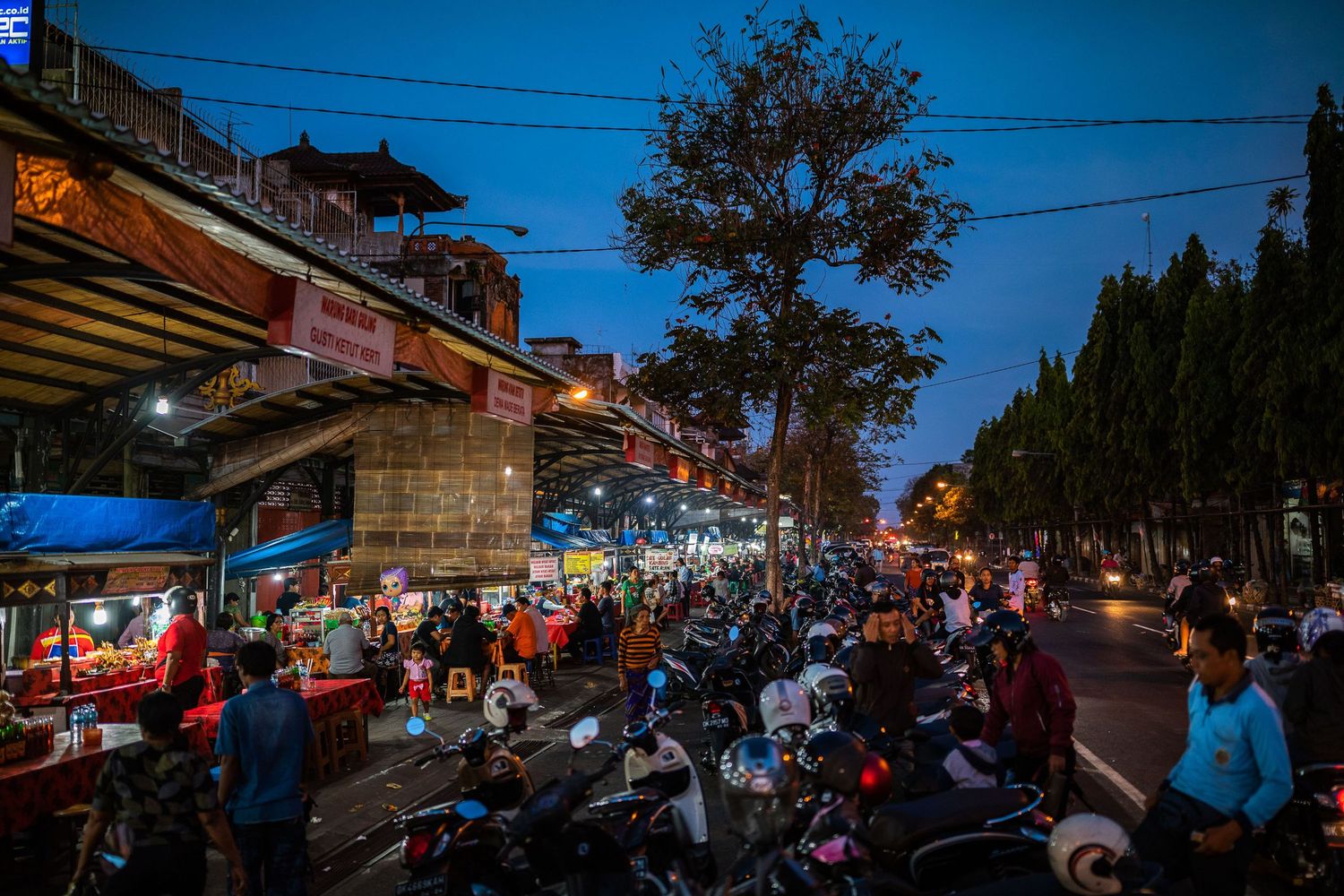 Panoramic view of a street market at dusk with blue sky and glowing lights.