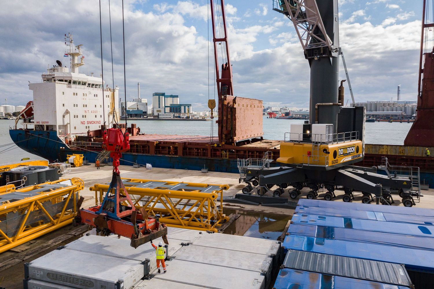 Large cargo containers being loaded at commercial shipping dock under blue skies.