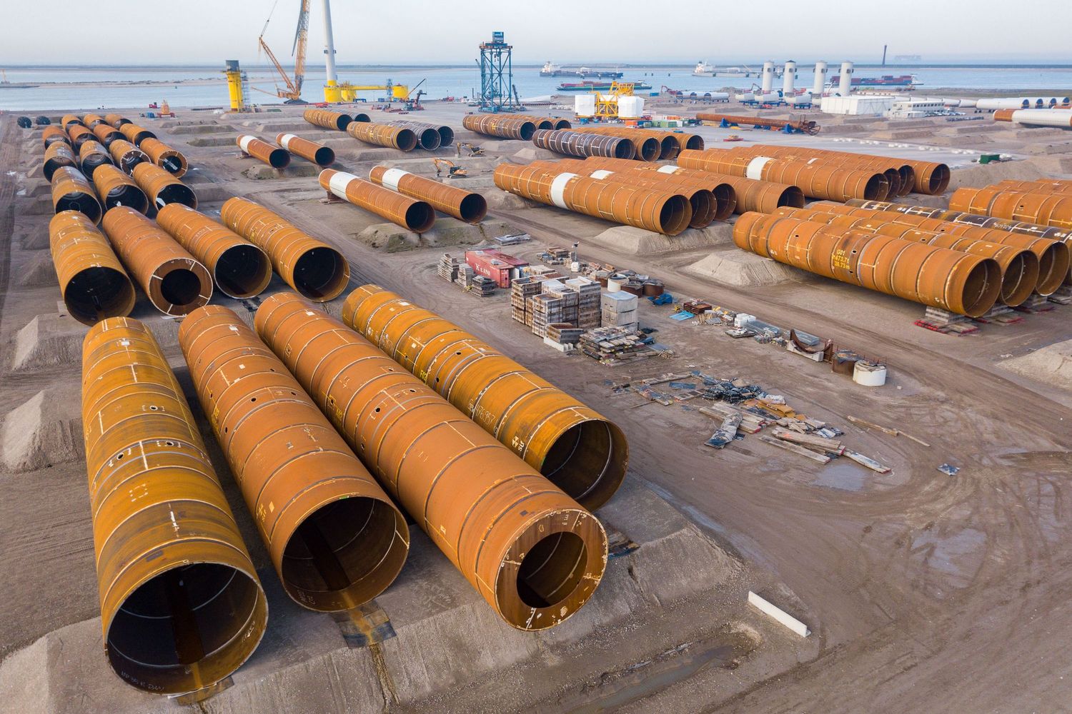 Large orange steel pipes and components laid out in rows at an industrial storage yard.